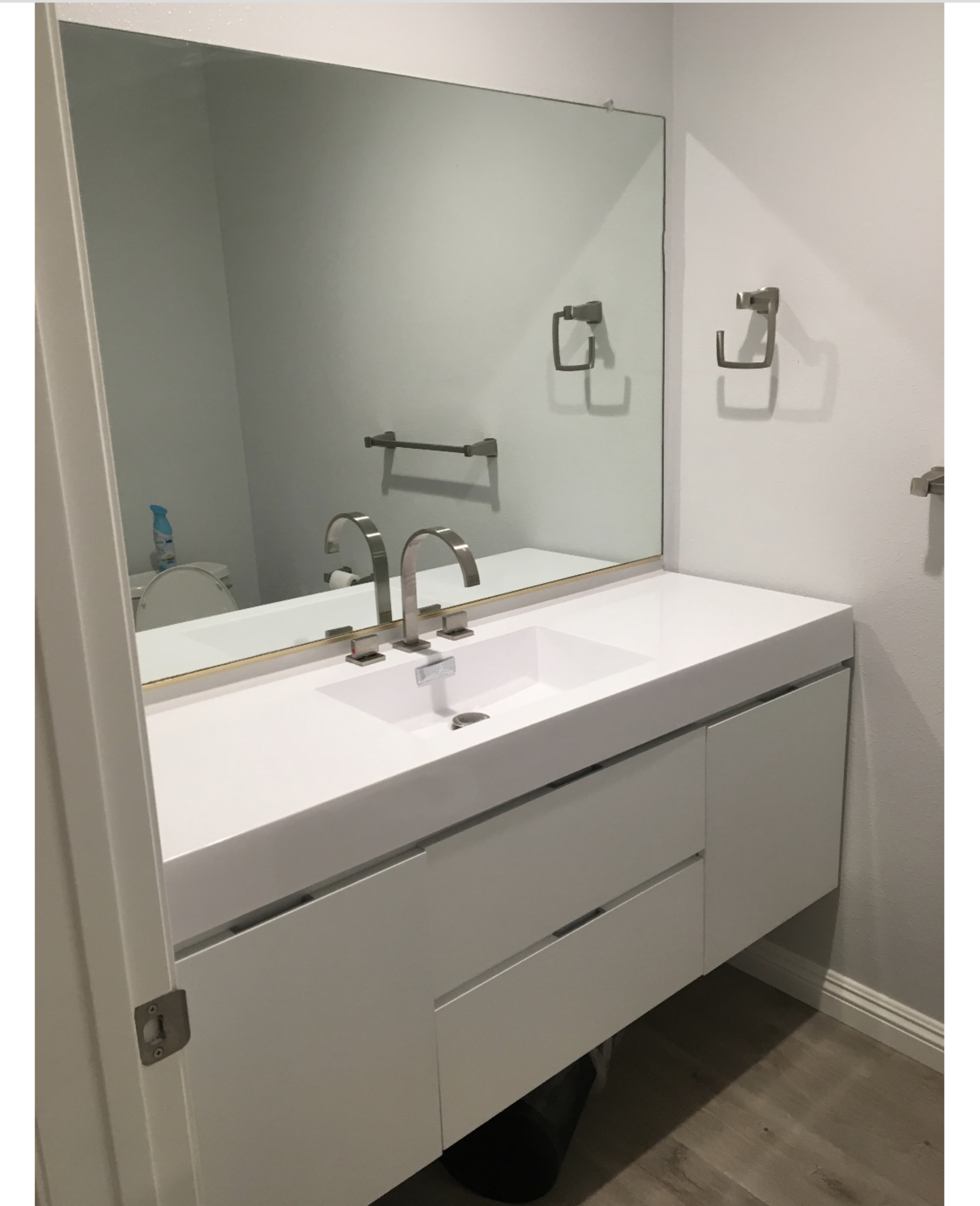 A modern bathroom with a white sink and a large mirror above it, complemented by minimal cabinetry and towel hooks on the wall.