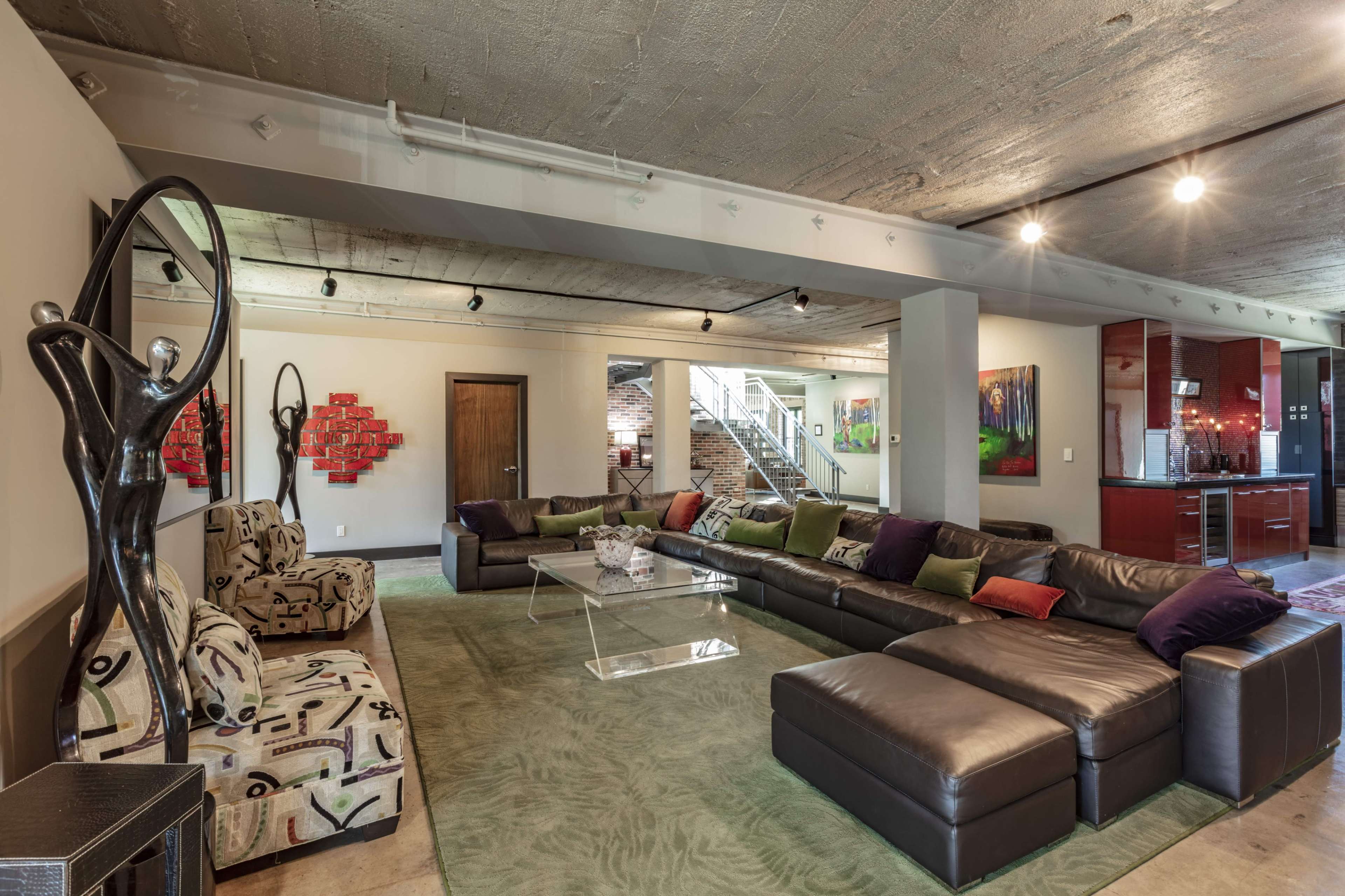 The spacious living room features a large sectional sofa, contemporary artwork, and a glass coffee table set on a green area rug.