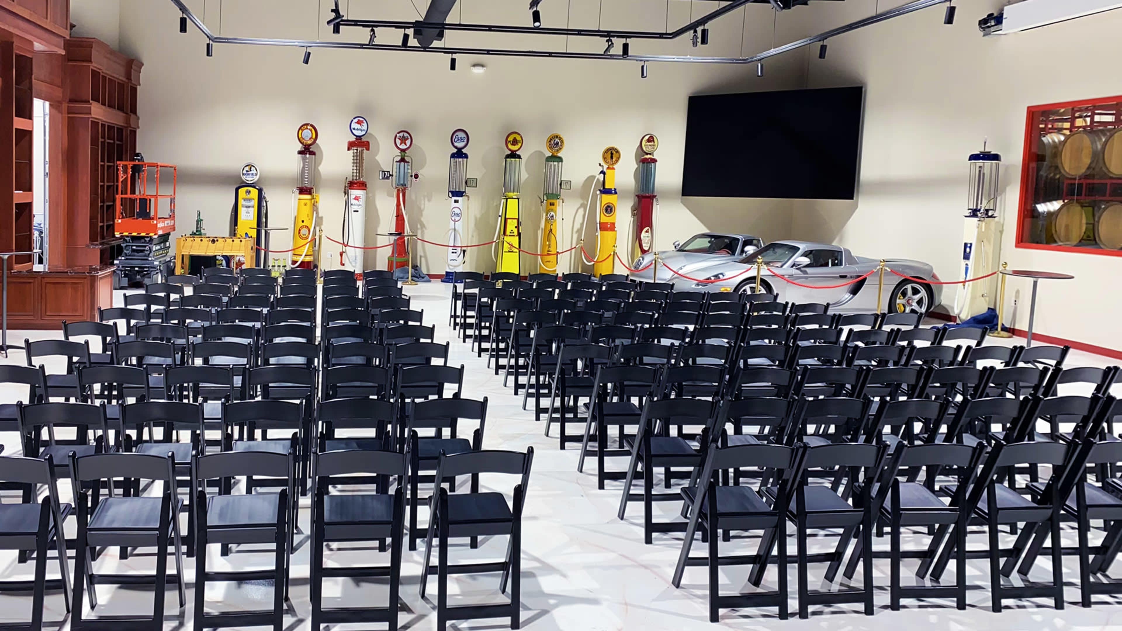 A neatly arranged auditorium with rows of black chairs facing a screen, surrounded by vintage gas pumps displayed on the walls.