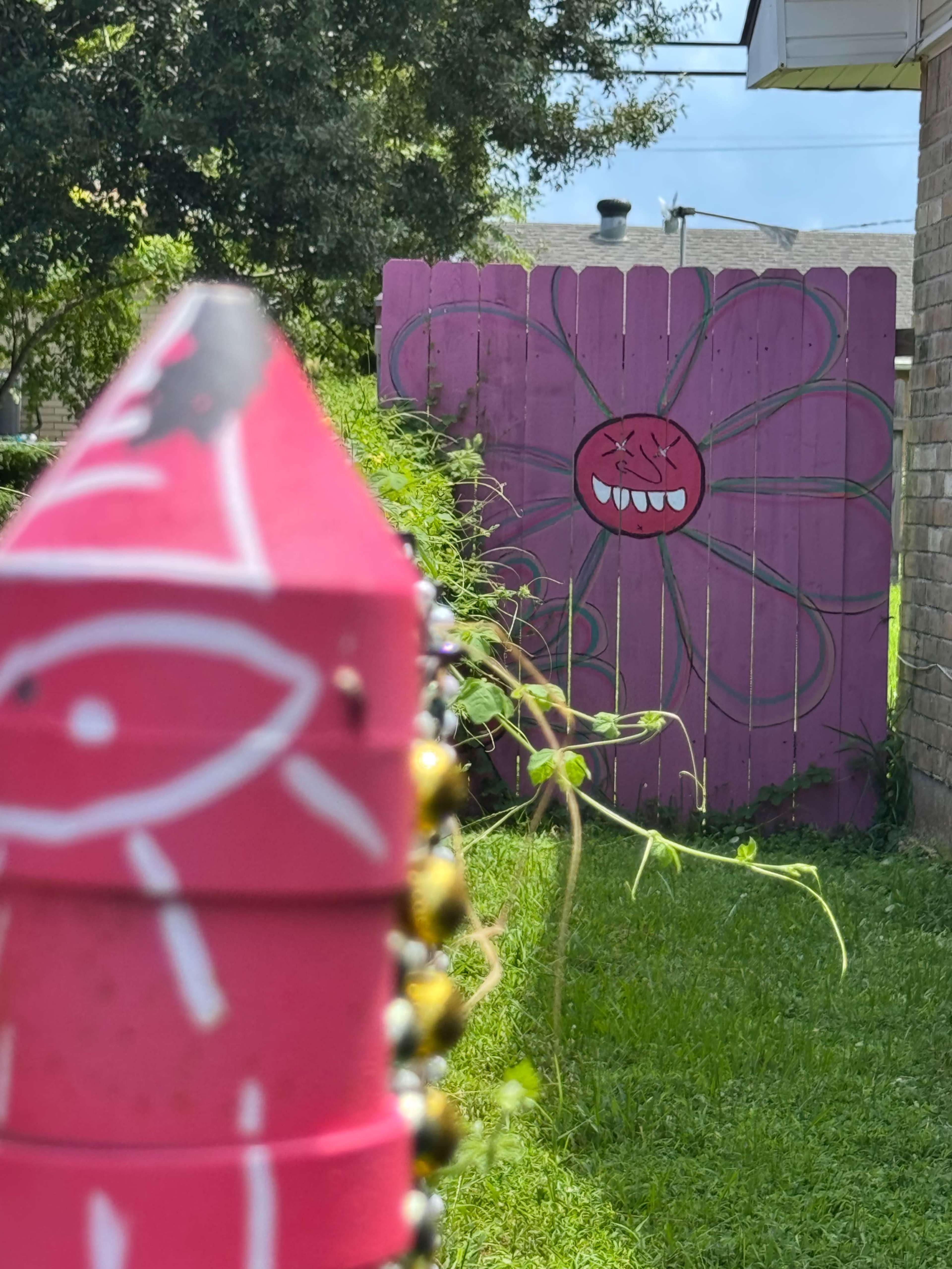 A colorful pink fence with a flower design is visible in a backyard, framed by a decorated pink stake in the foreground.