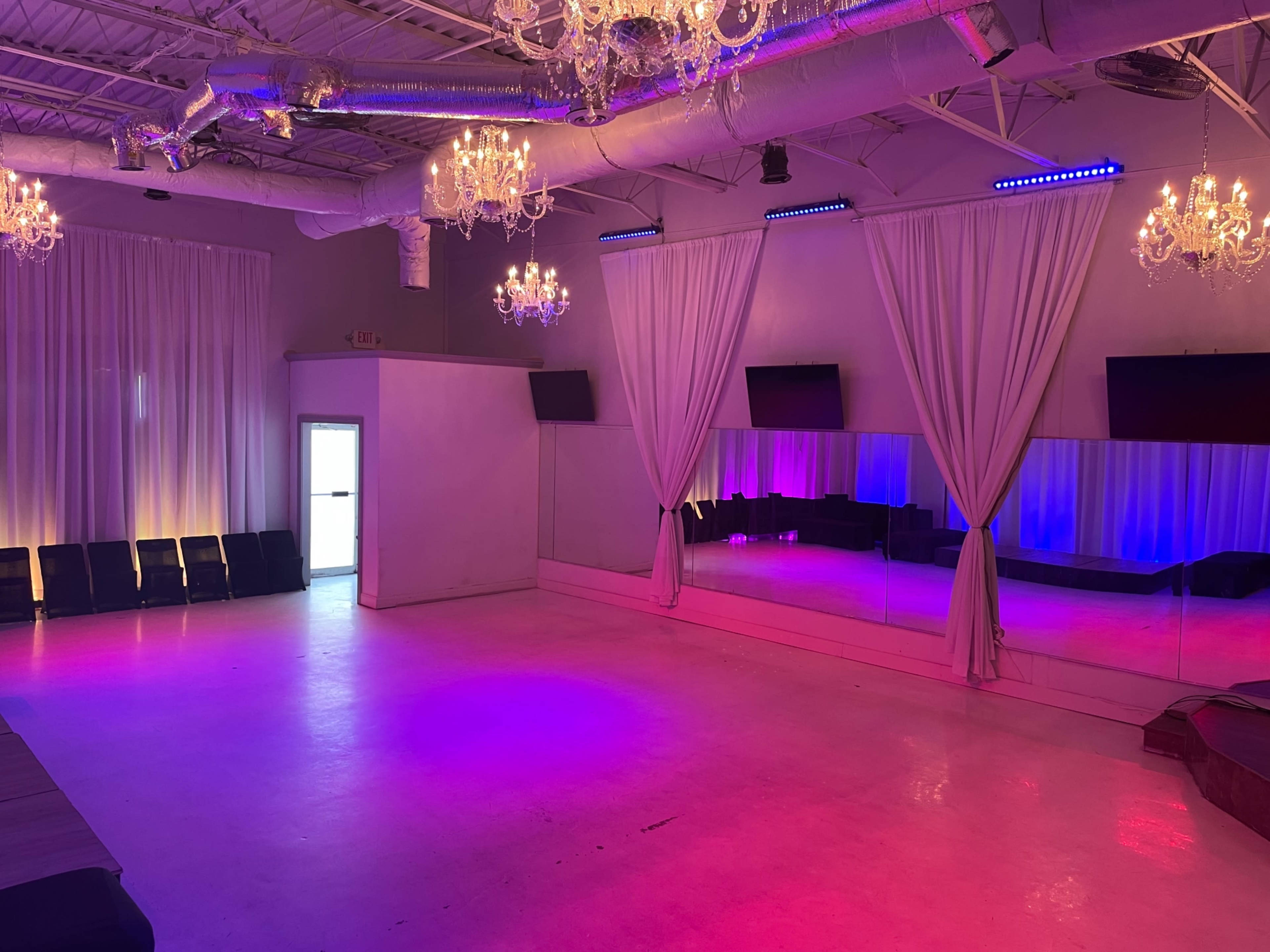 The room features a spacious dance floor with mirrored walls, draped curtains, and chandeliers, illuminated by colorful lights.