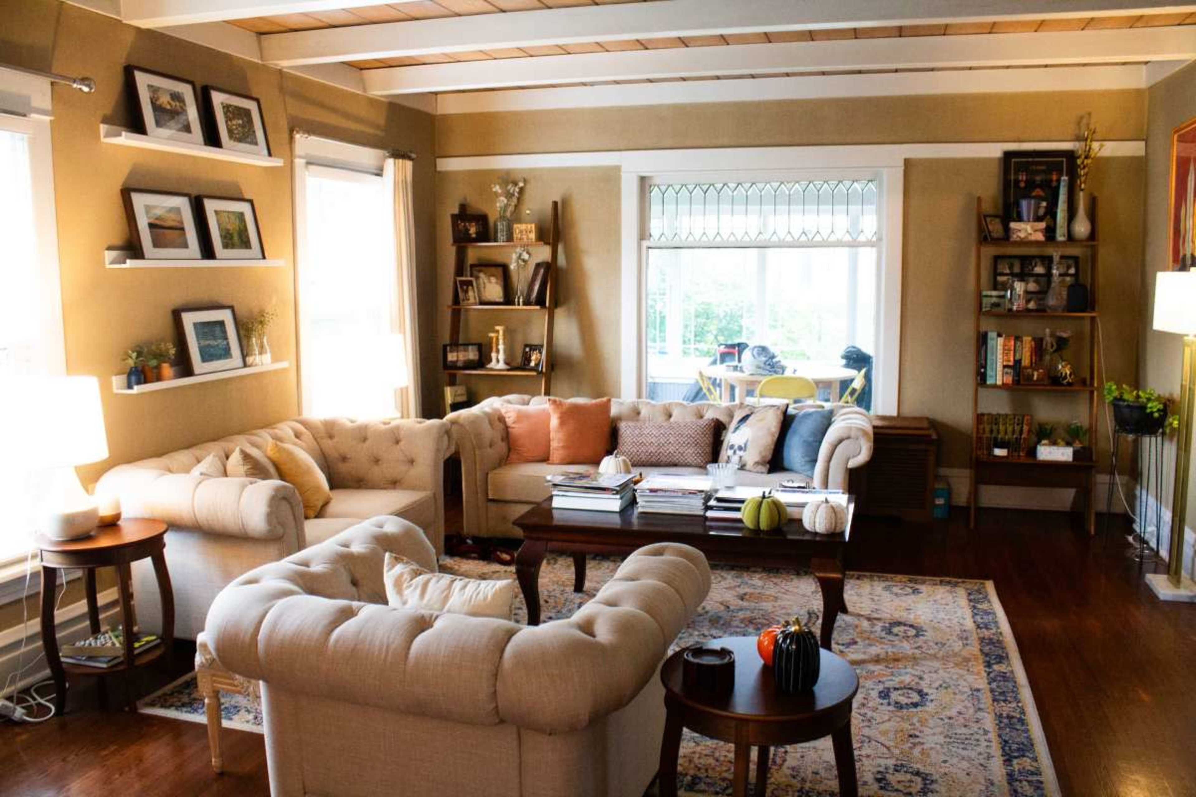 A cozy living room featuring a light-colored sectional sofa, a wooden coffee table, and a large window with decorative trim.