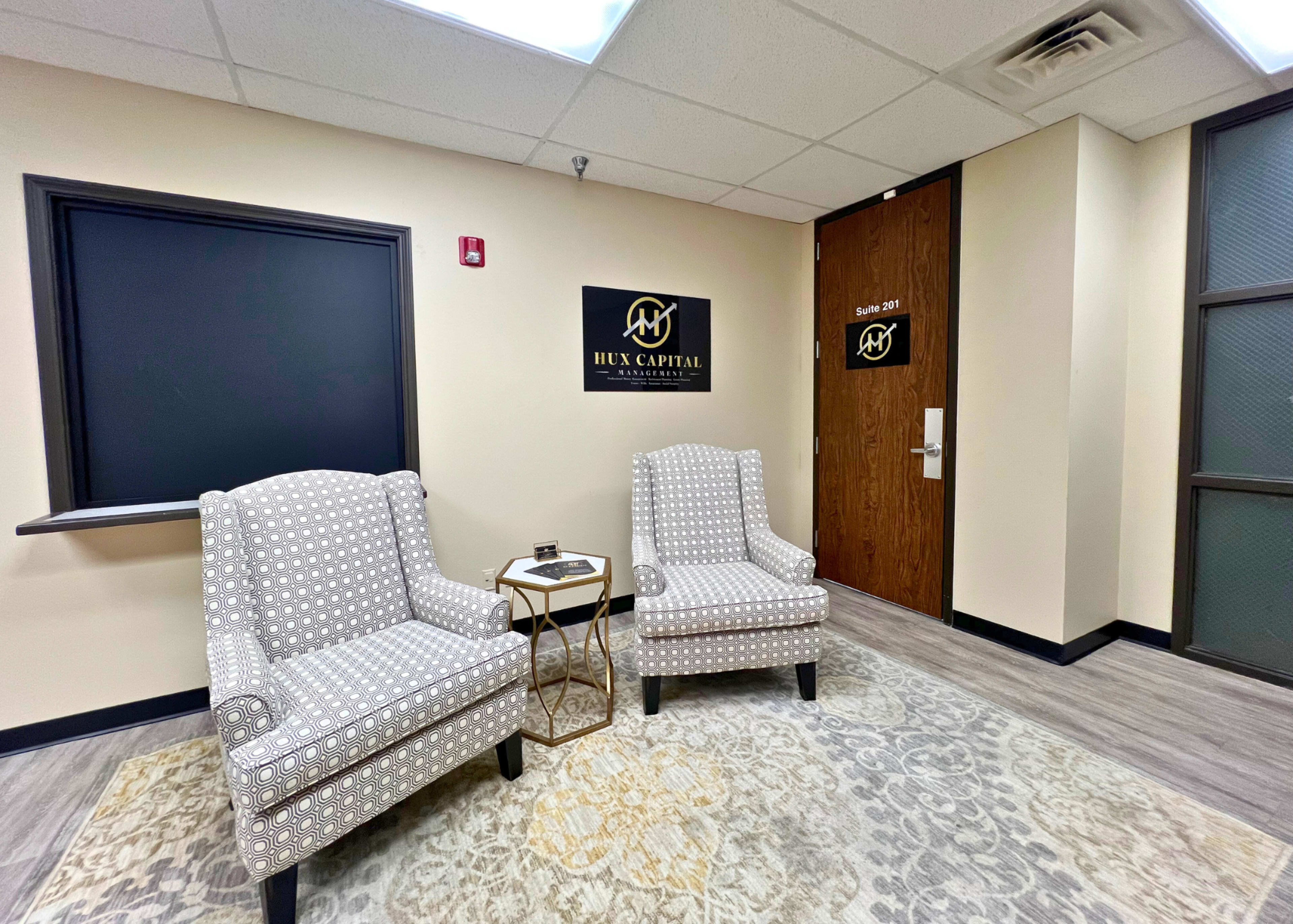 A small waiting area with two upholstered chairs, a side table, and a door labeled "HUX CAPITAL."