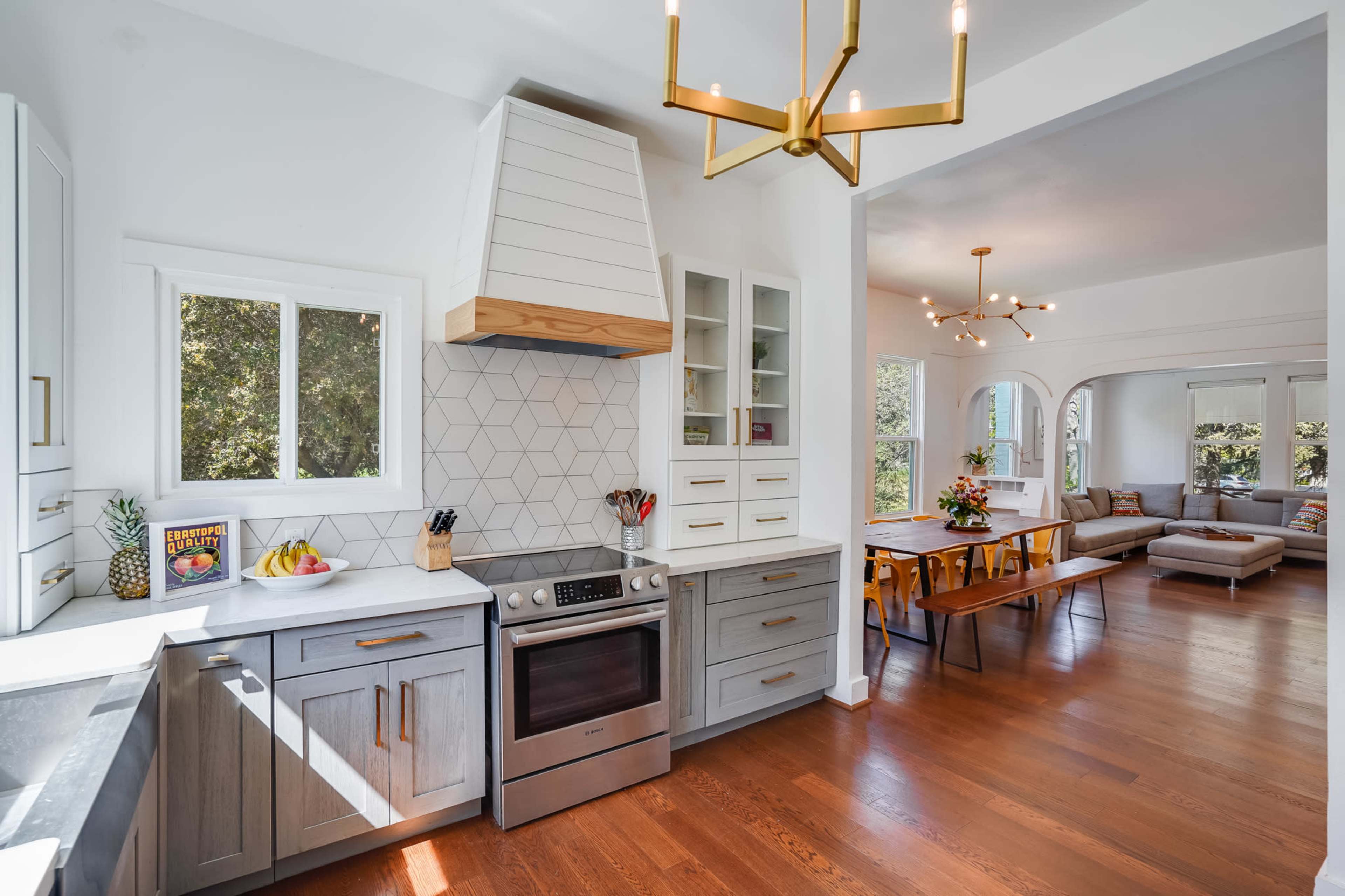 A modern kitchen features a stainless steel oven, a geometric tile backsplash, and a large island with natural light streaming through the windows.