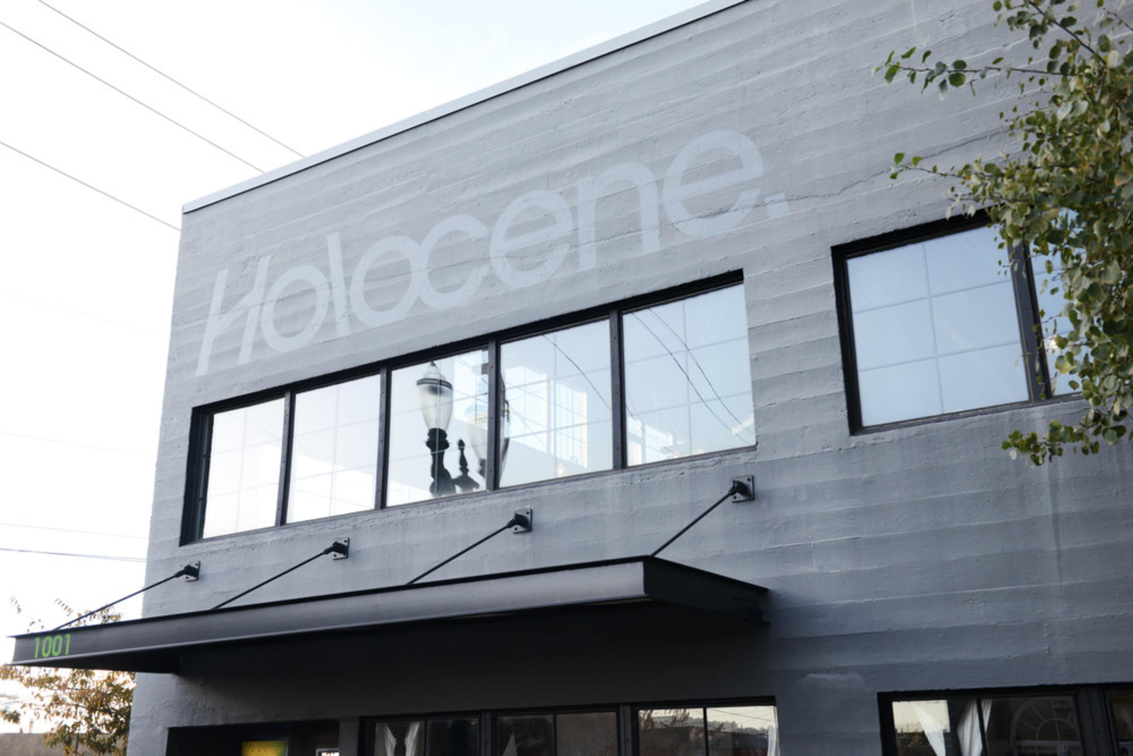 The exterior of a gray building features large windows and the word "Holocene" prominently displayed on the upper wall.