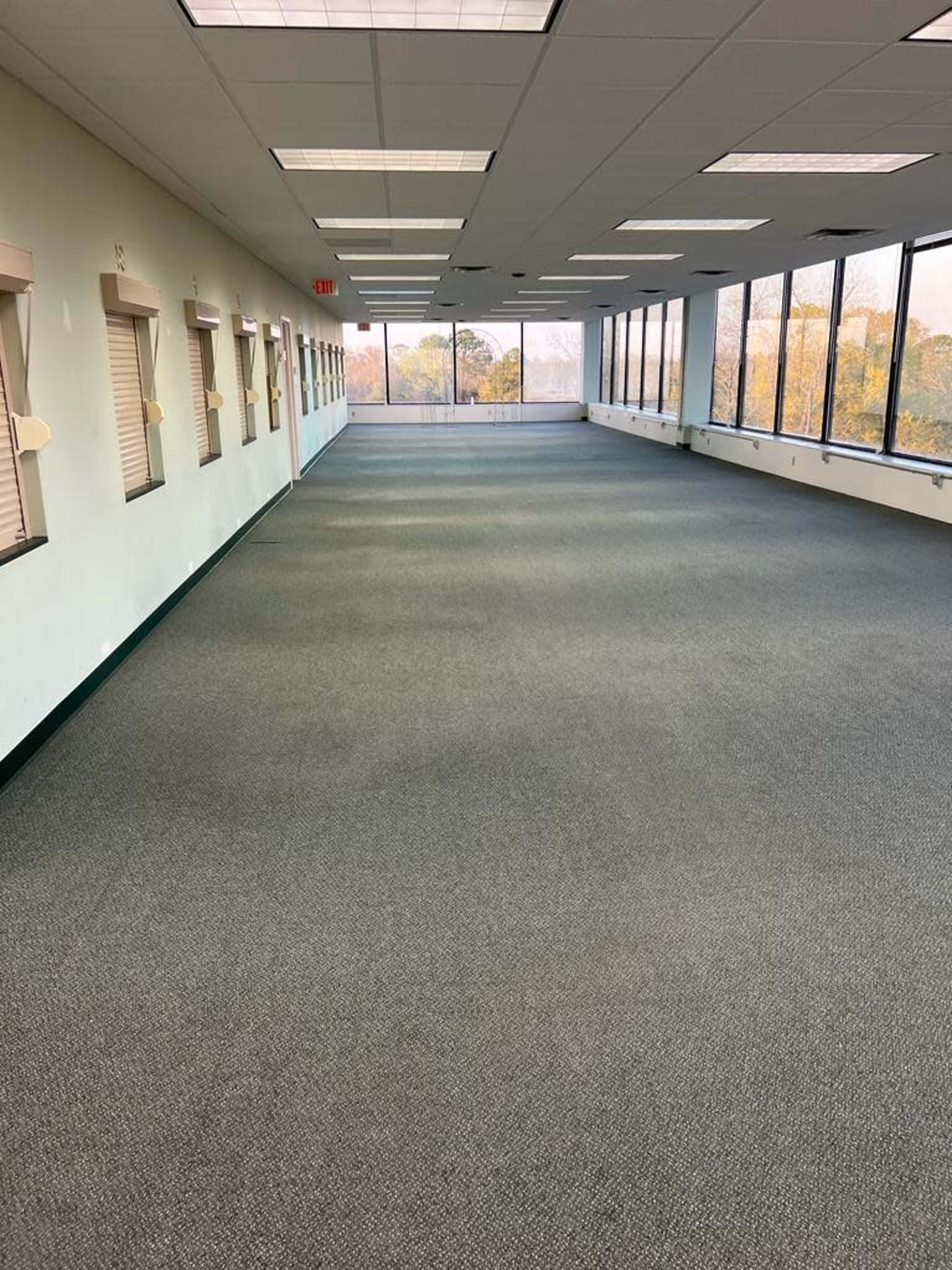 The image shows an empty hallway with large windows on one side and a carpeted floor.