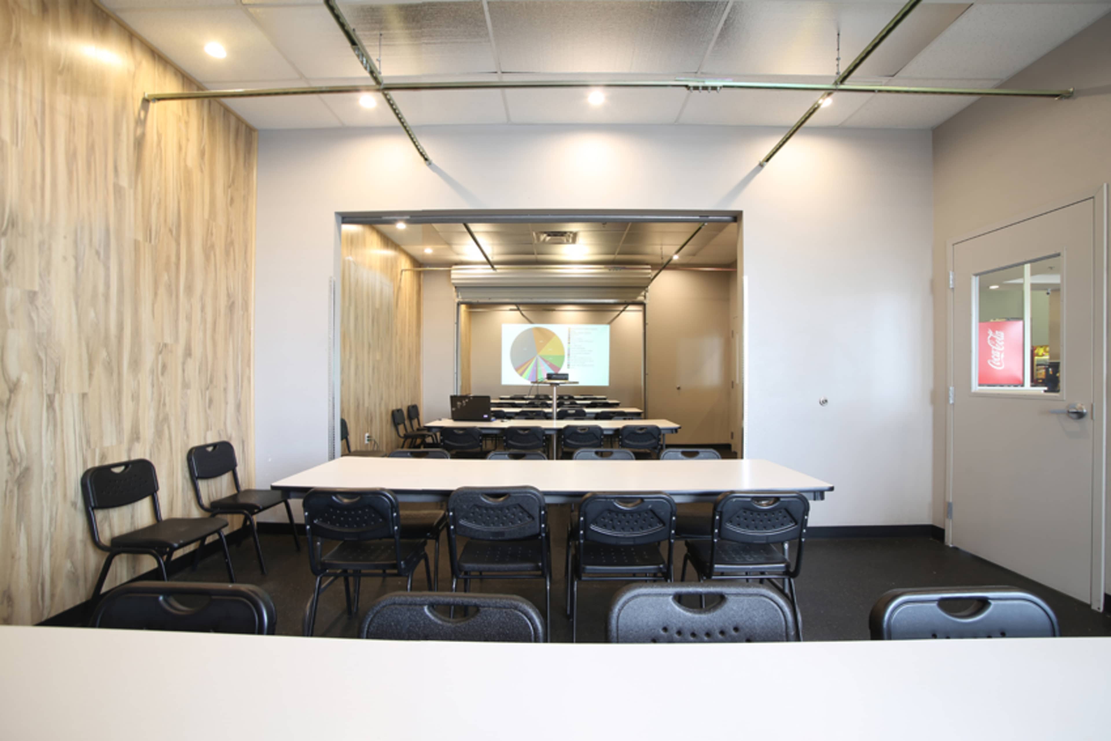 The image shows a conference room with multiple rows of black chairs and a projector screen displaying a pie chart.
