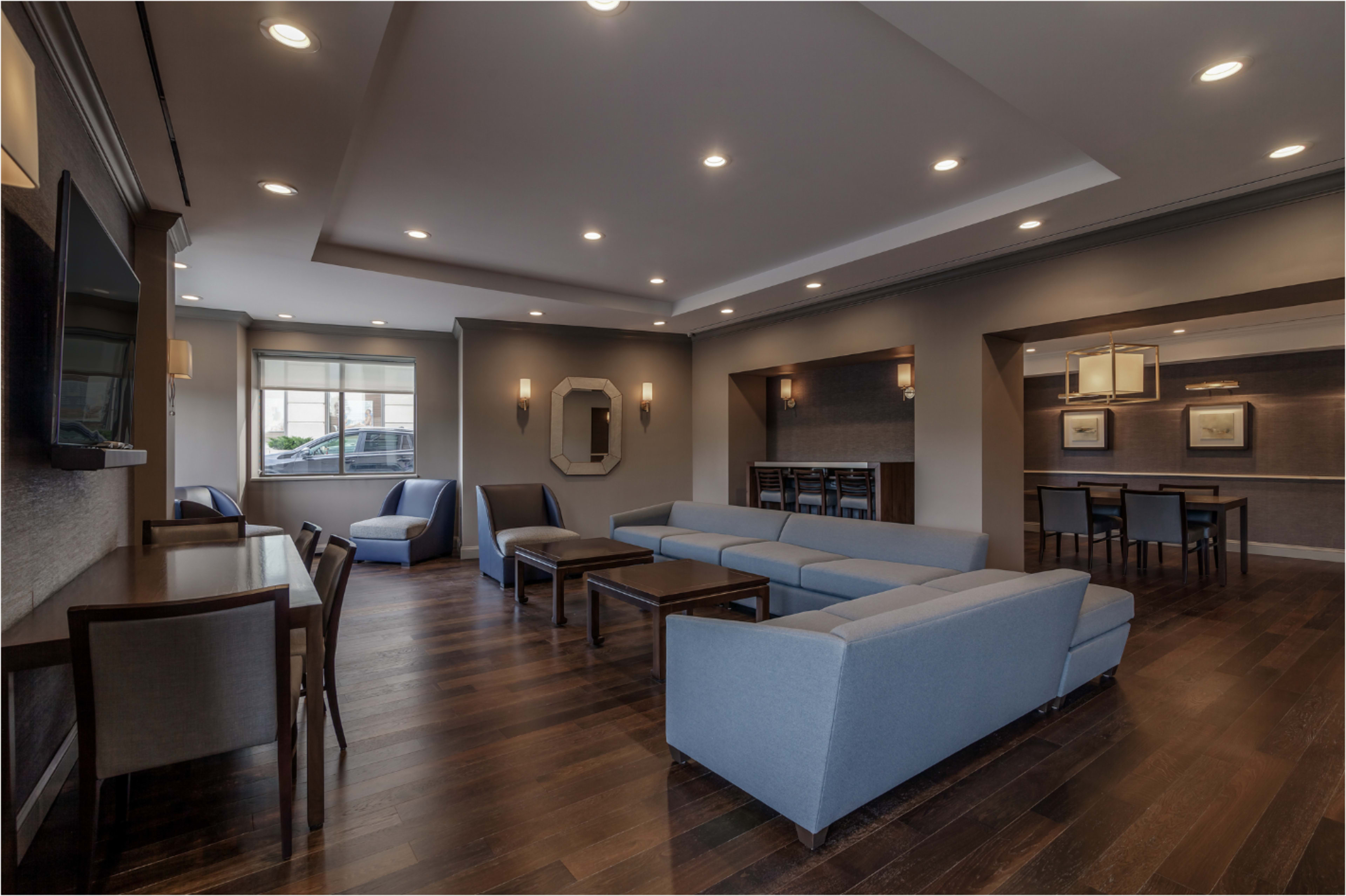 The image shows a modern lounge area featuring blue furniture, hardwood floors, and various seating arrangements alongside tables in a well-lit space.