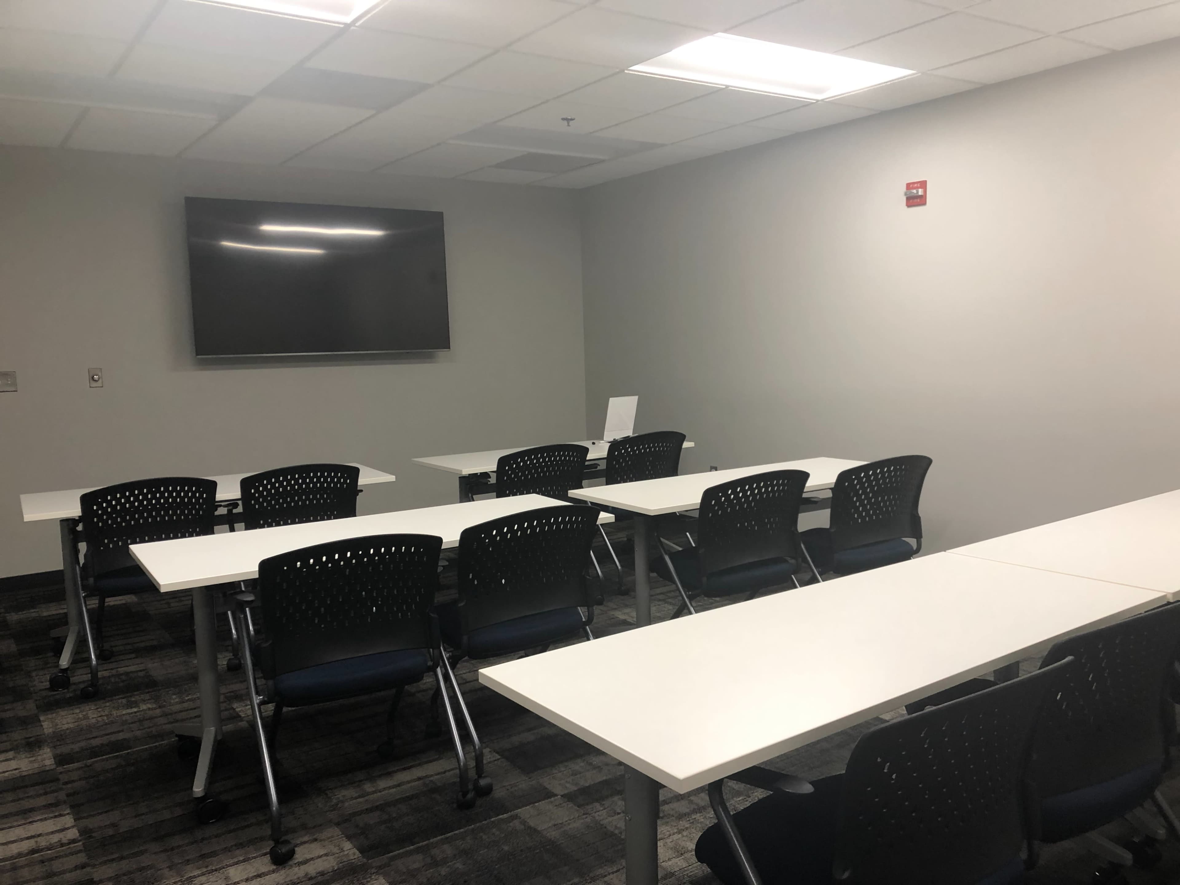 A conference room with several tables and chairs arranged facing a wall-mounted television.
