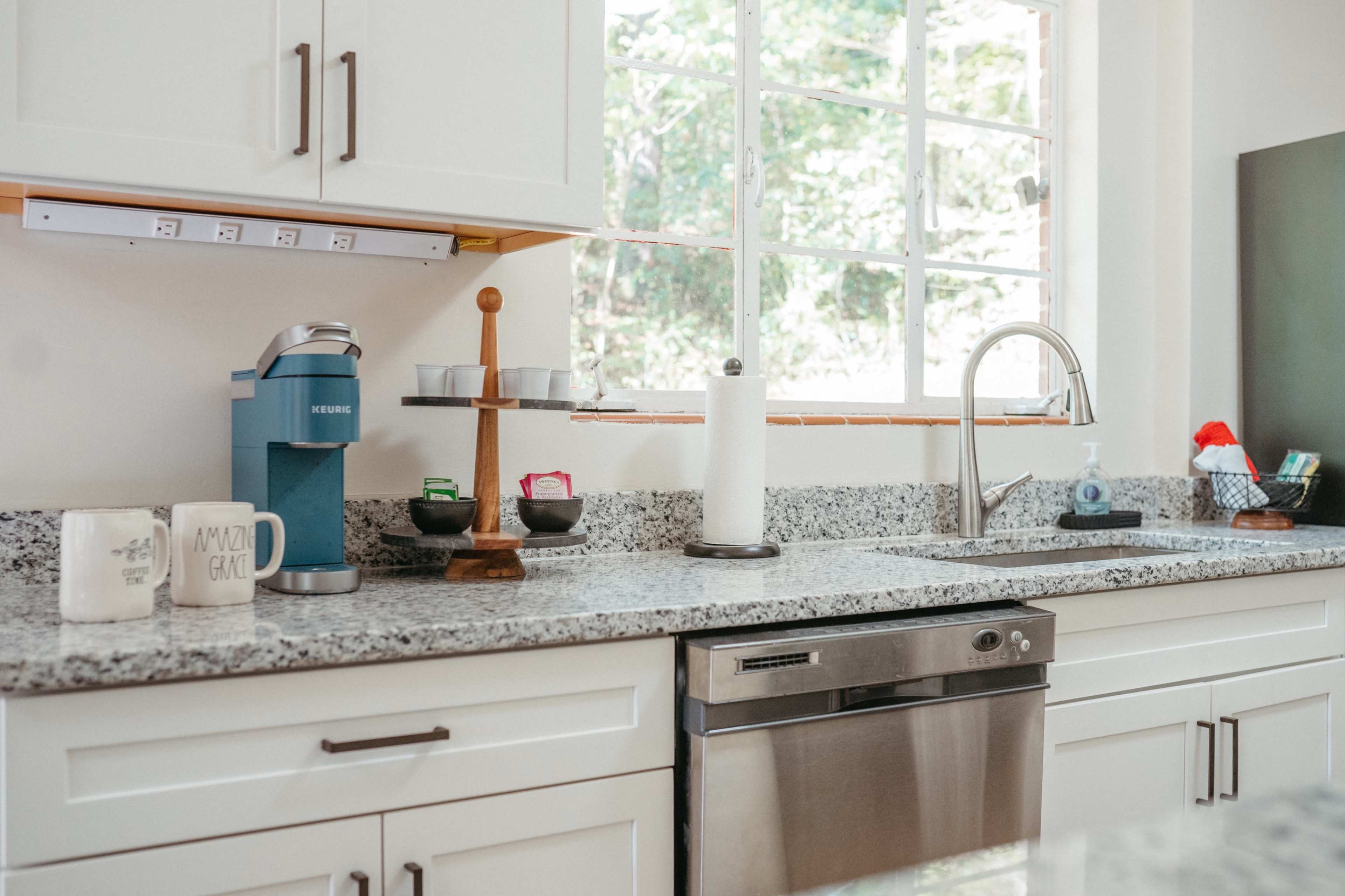 The image shows a modern kitchen countertop with a coffee maker, a paper towel holder, and various kitchen items near a window.