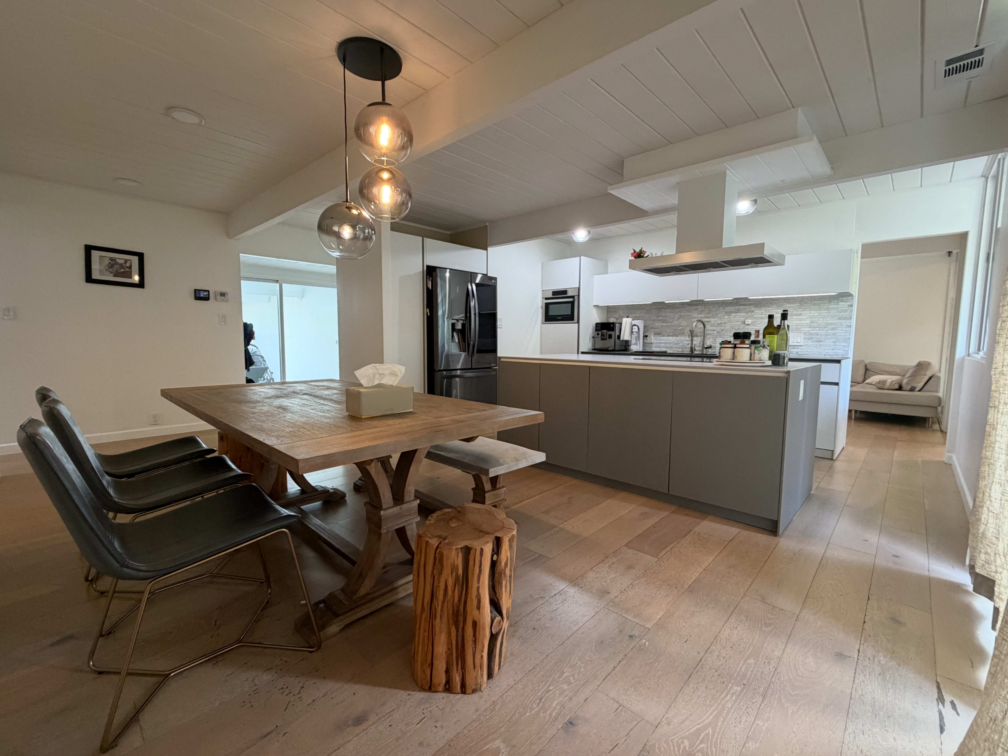 A modern kitchen and dining area feature a wooden table with metal chairs, a stone backsplash, and sleek appliances.