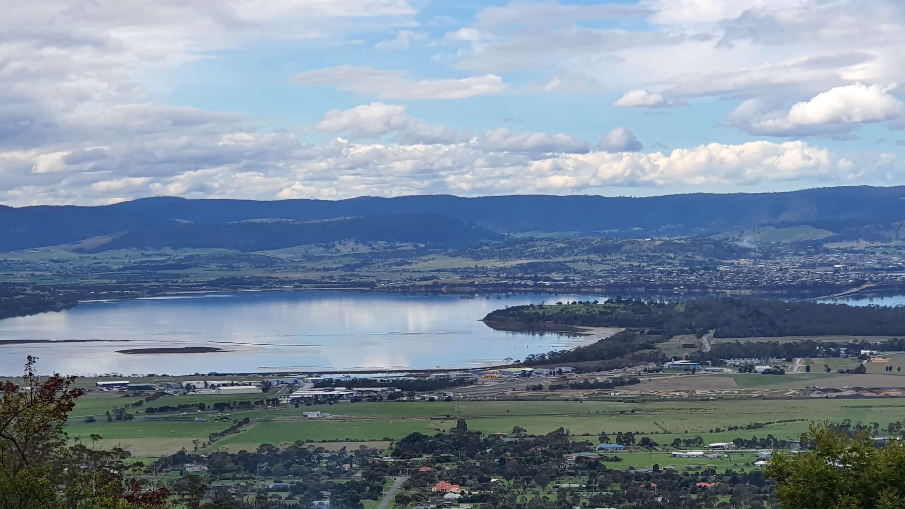 A landscape featuring a large lake surrounded by hills and farmland under a partly cloudy sky.