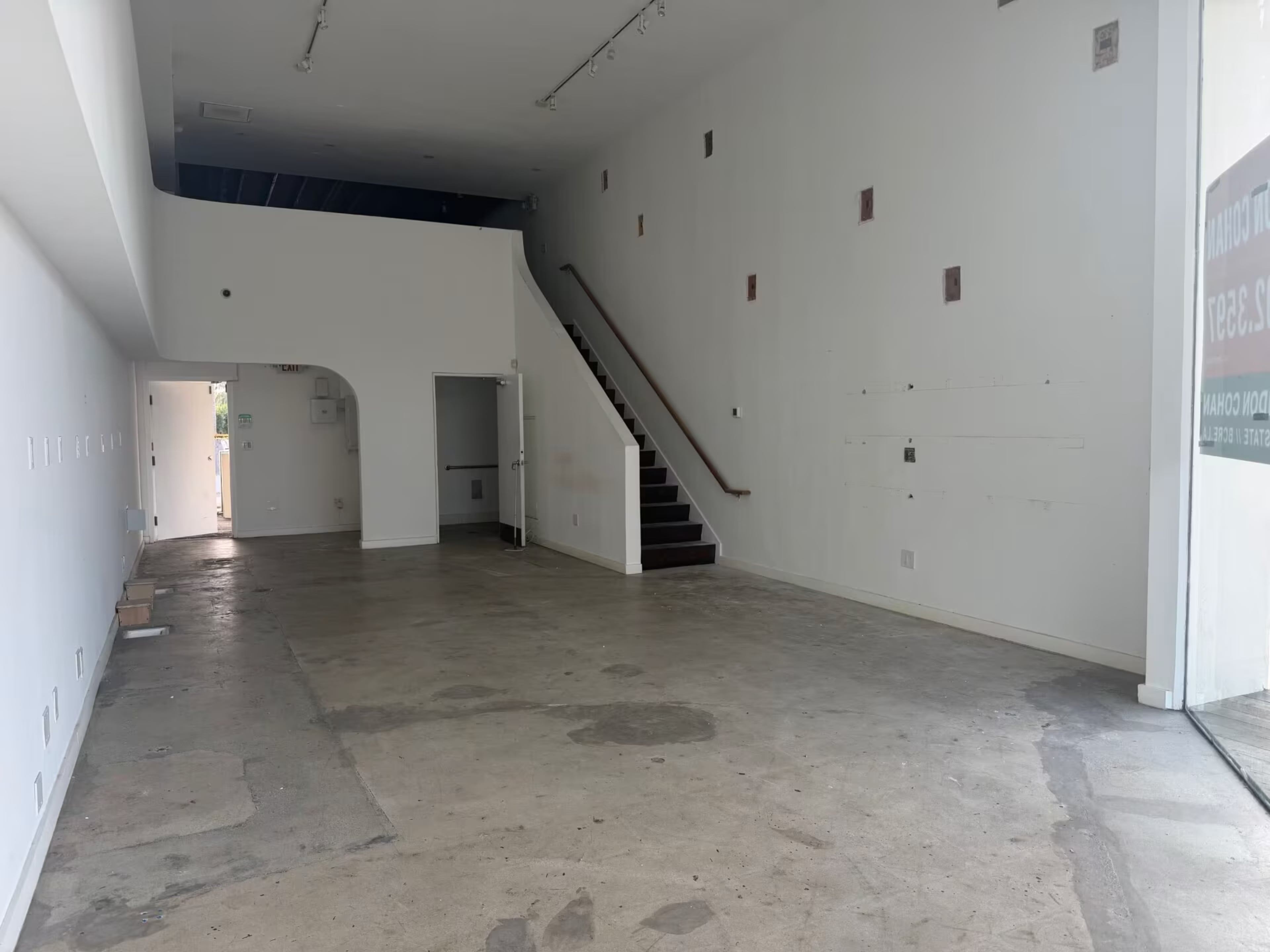 The image shows an empty retail space featuring a staircase on the left and unadorned white walls.