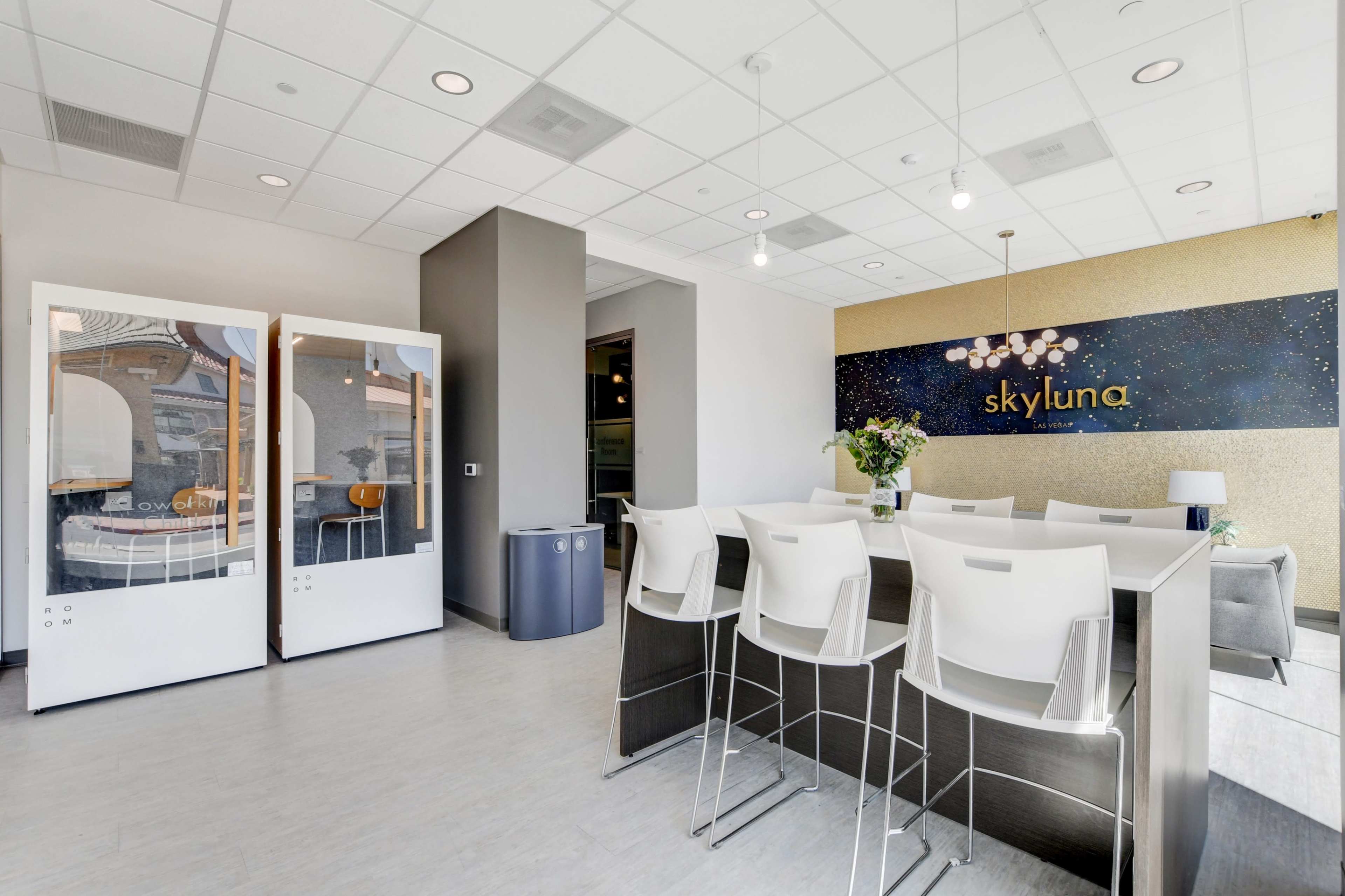 A modern office space with a reception area, featuring a large table, white chairs, a decorated wall with the name "skyluna," and glass partitions.