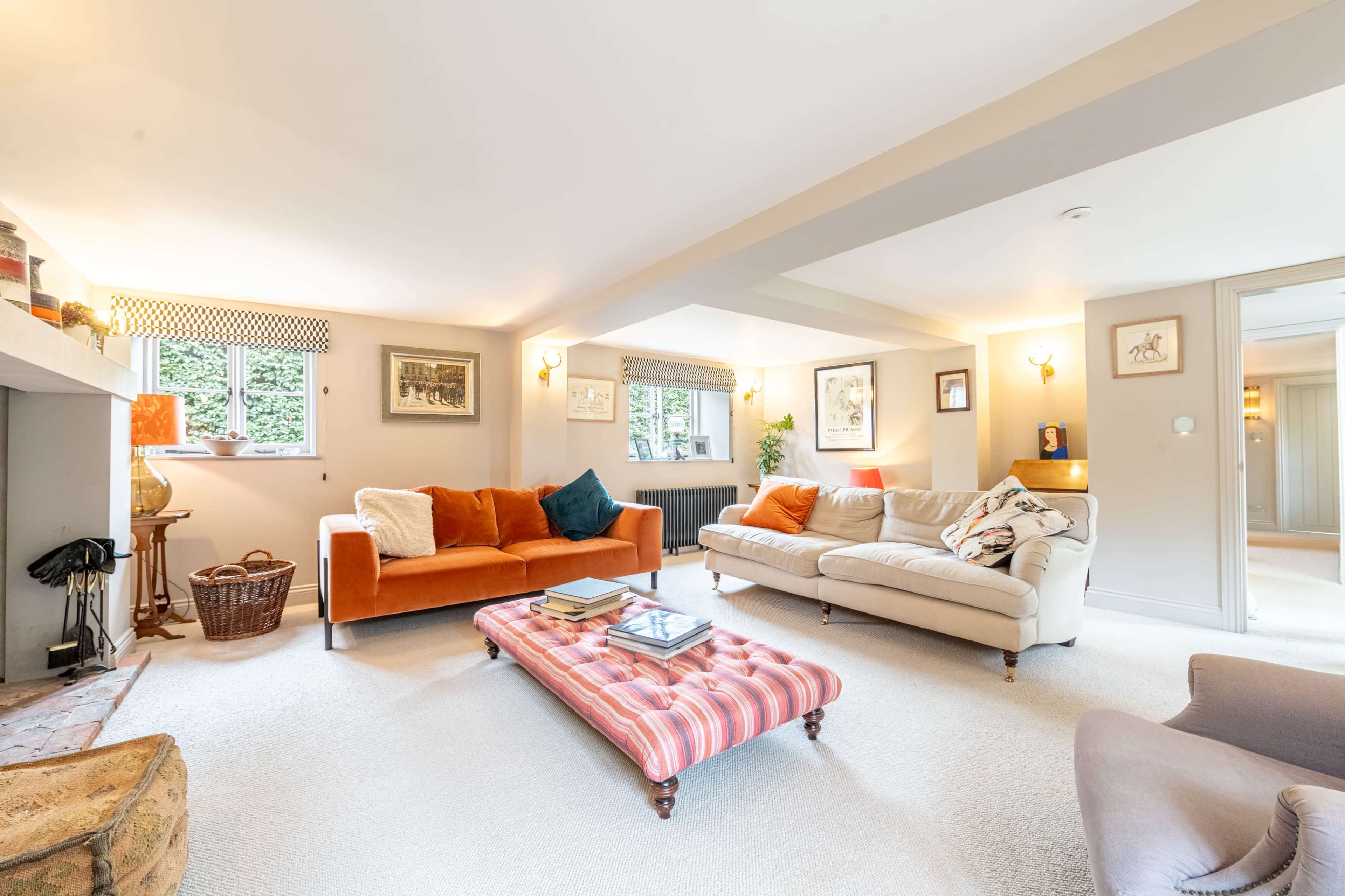 A spacious living room with a mix of seating options, including a striped coffee table and large windows revealing greenery outside.