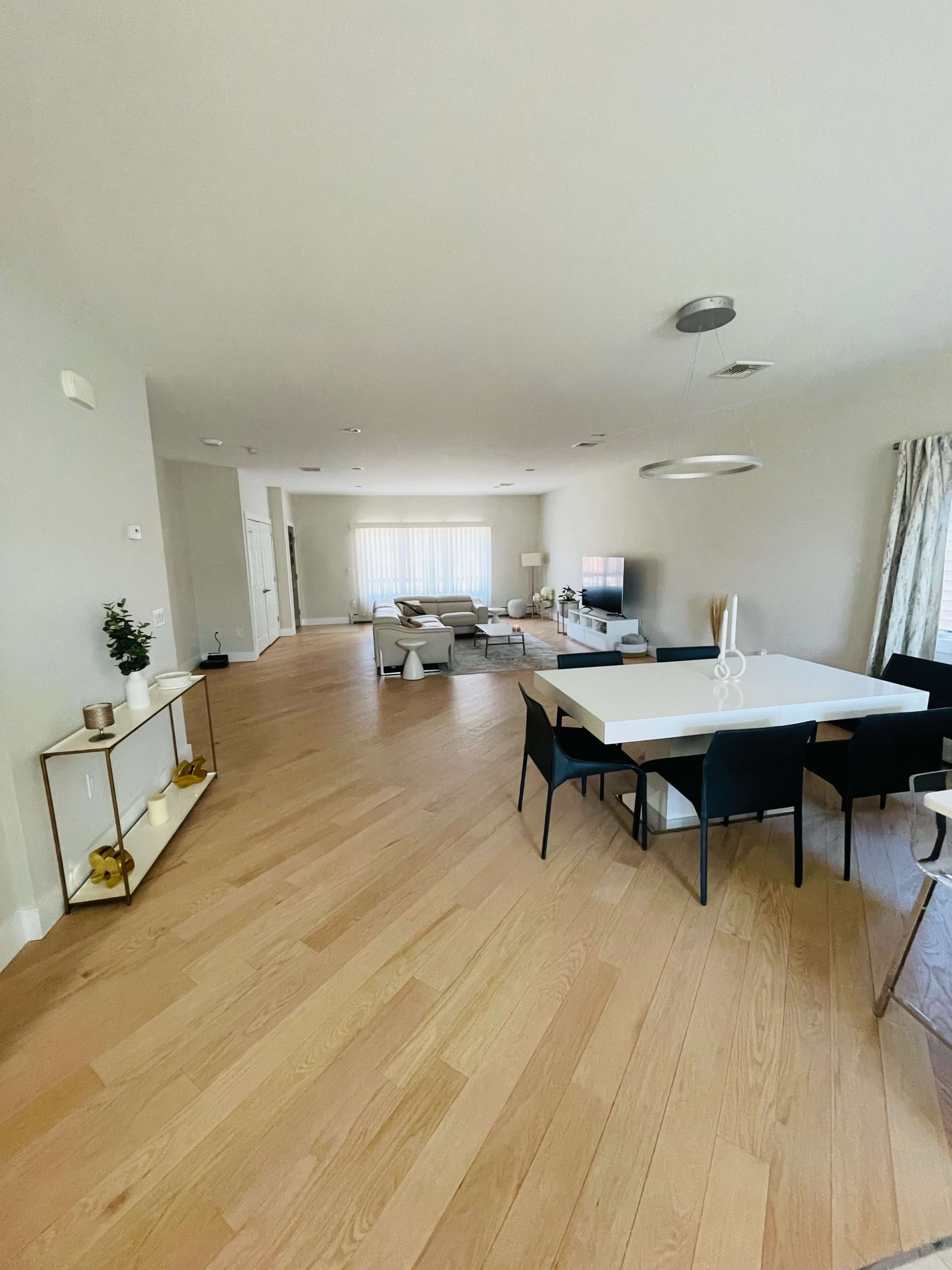 A modern living and dining area with light wood flooring, a large dining table surrounded by black chairs, and a cozy seating arrangement in front of a television.