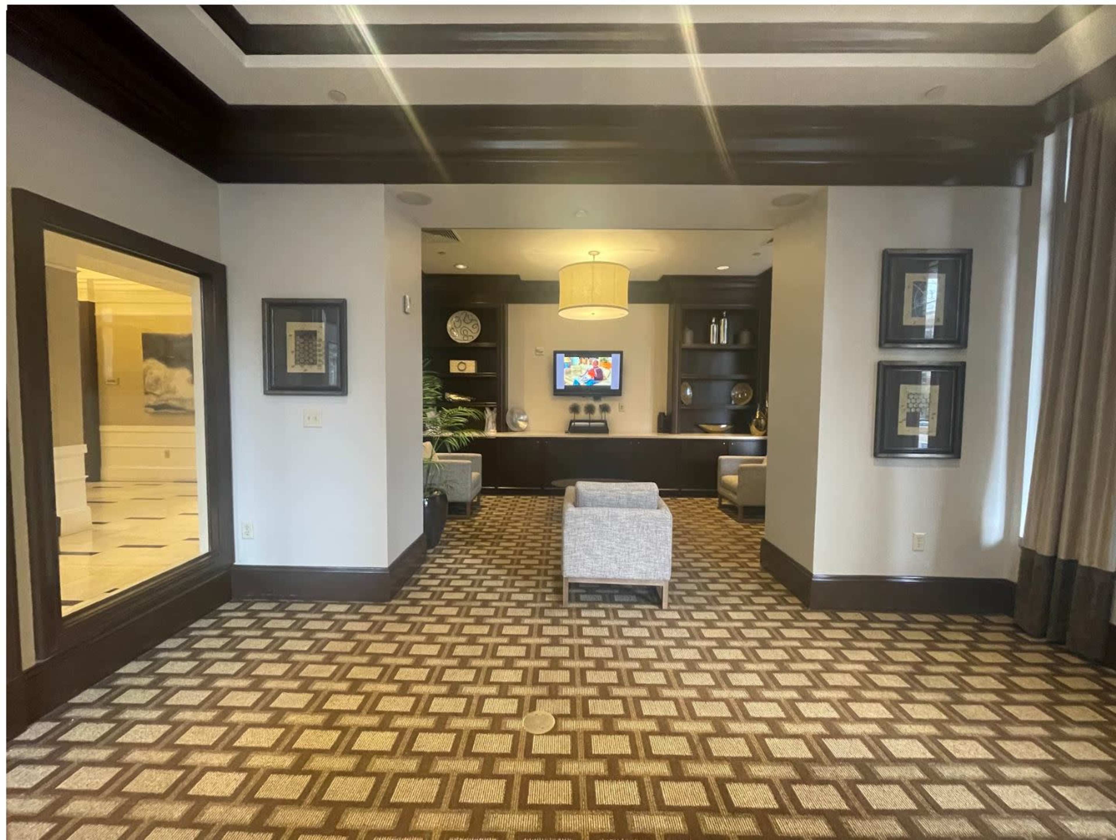 A spacious lobby area with patterned carpet, dark wood accents, and a wall-mounted television flanked by modern seating arrangements.