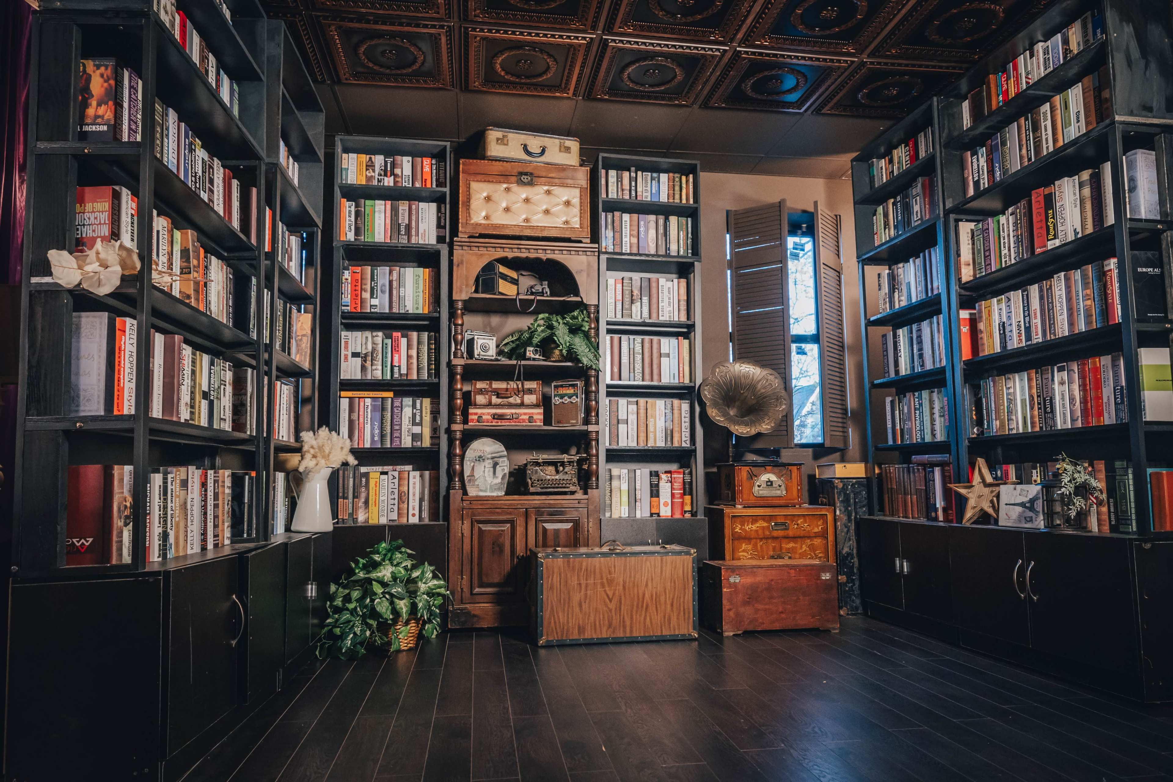 A cozy library with tall bookshelves filled with books, an antique gramophone, and various decorative items, all arranged around a wooden cabinet.