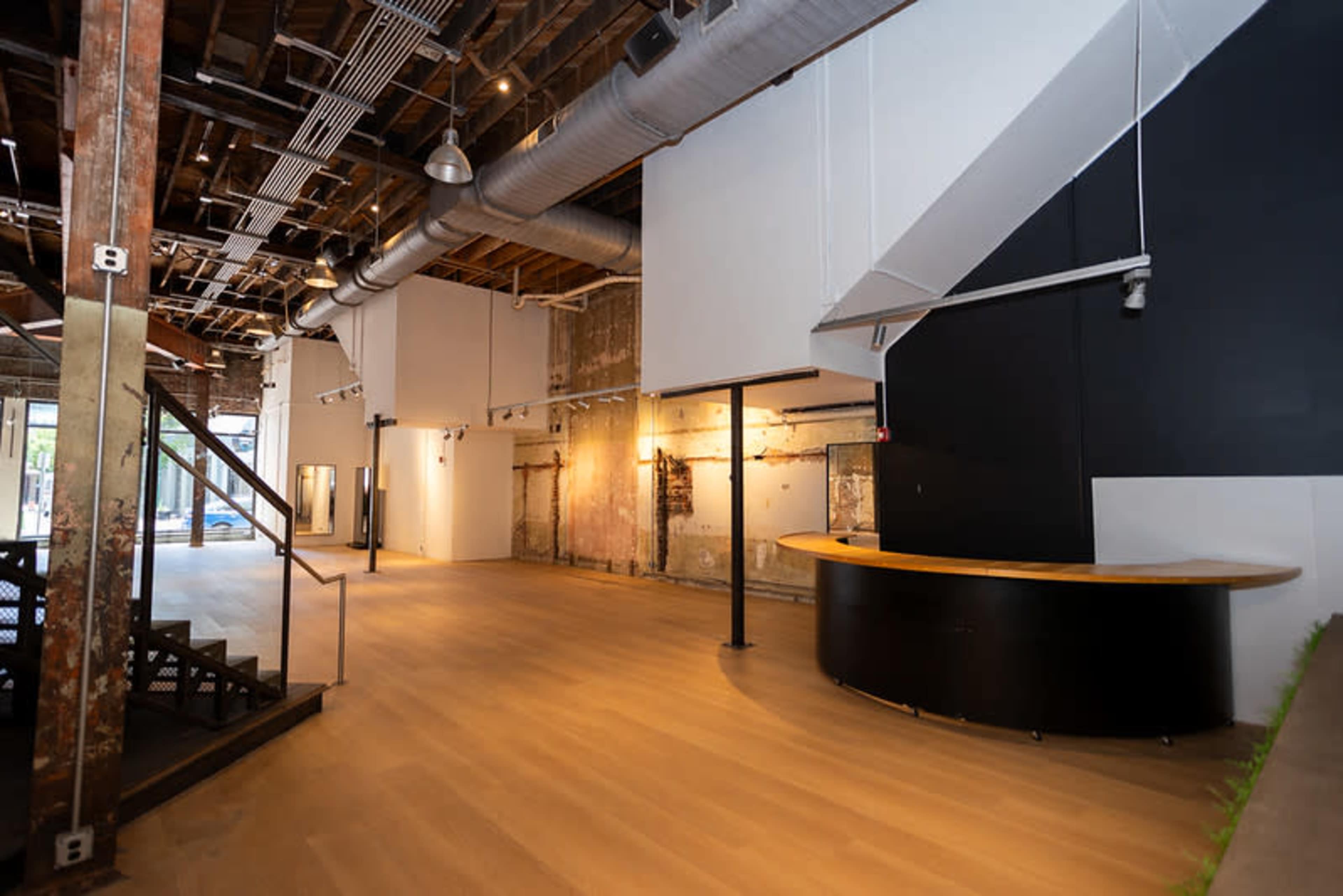The image shows an empty, modern commercial space featuring wooden flooring, exposed beams, and a curved reception desk.