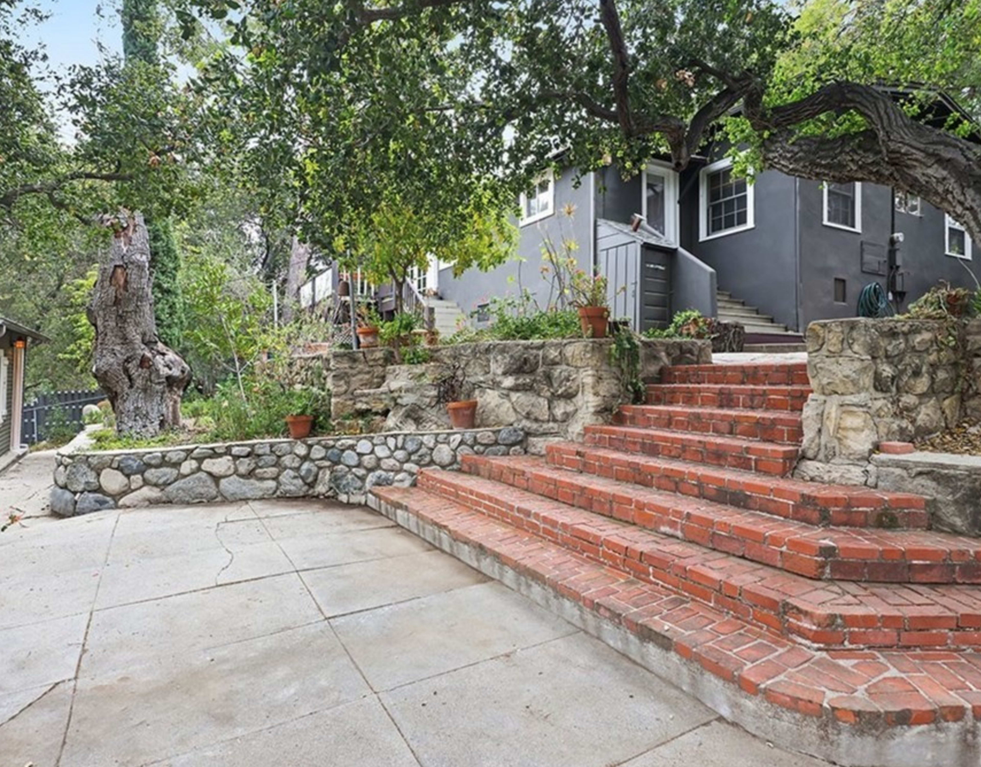 A stone terrace with a set of brick steps leading up to a building surrounded by greenery and potted plants.