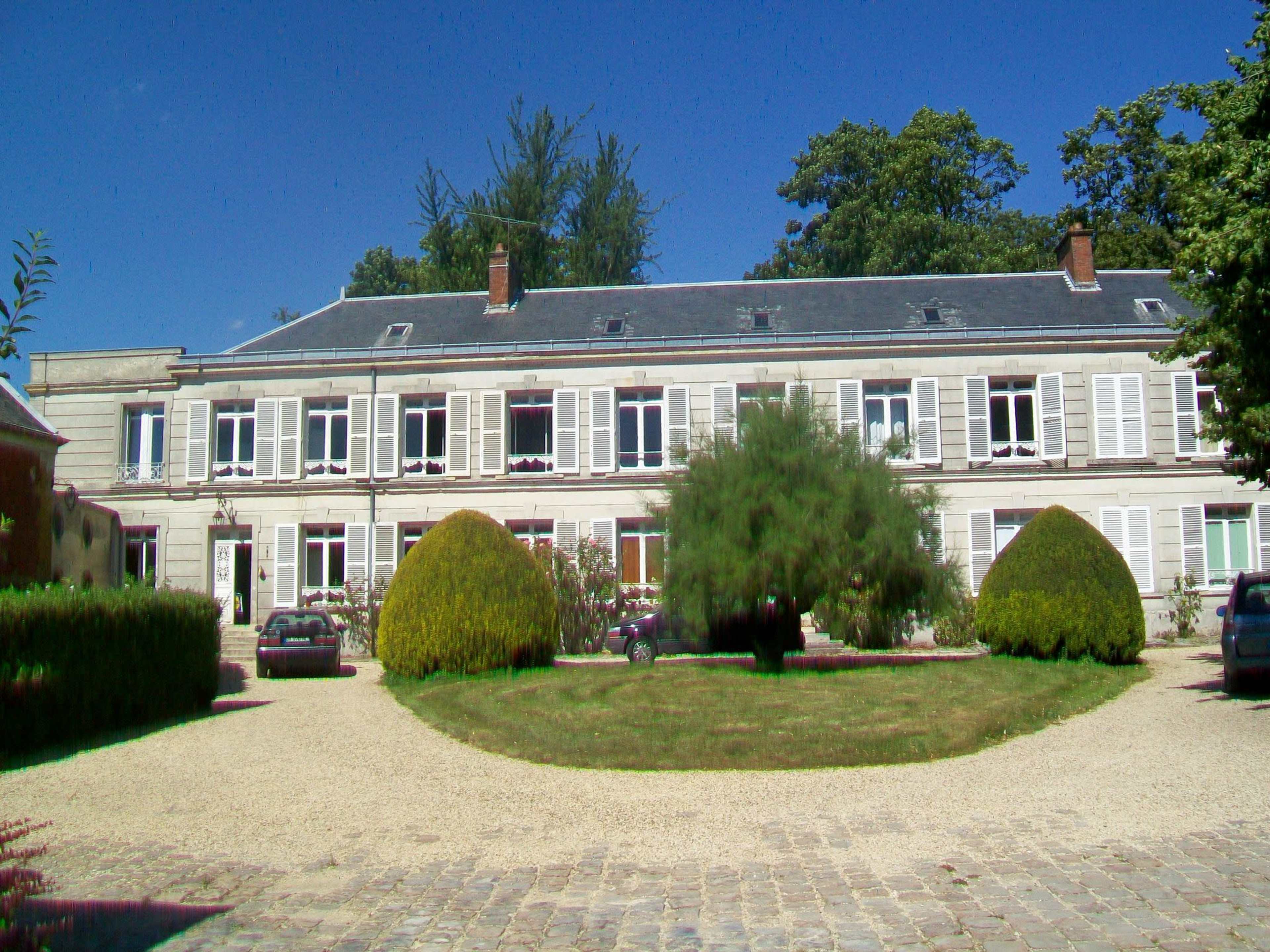 A large, two-story house with multiple windows and a symmetrical landscape featuring trimmed bushes and a gravel driveway.