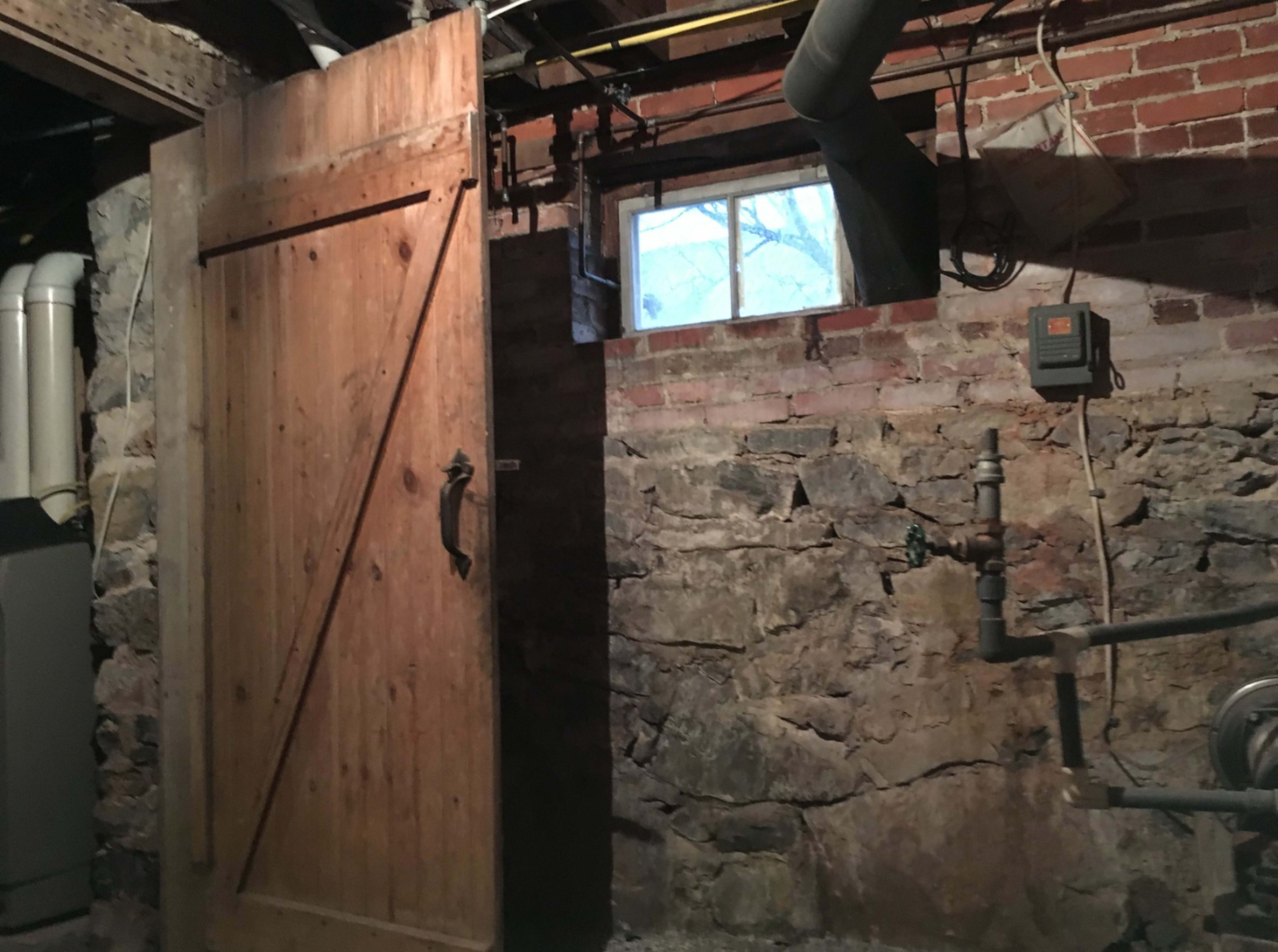 A wooden barn door partially open in a dimly lit basement with exposed brick and stone walls.