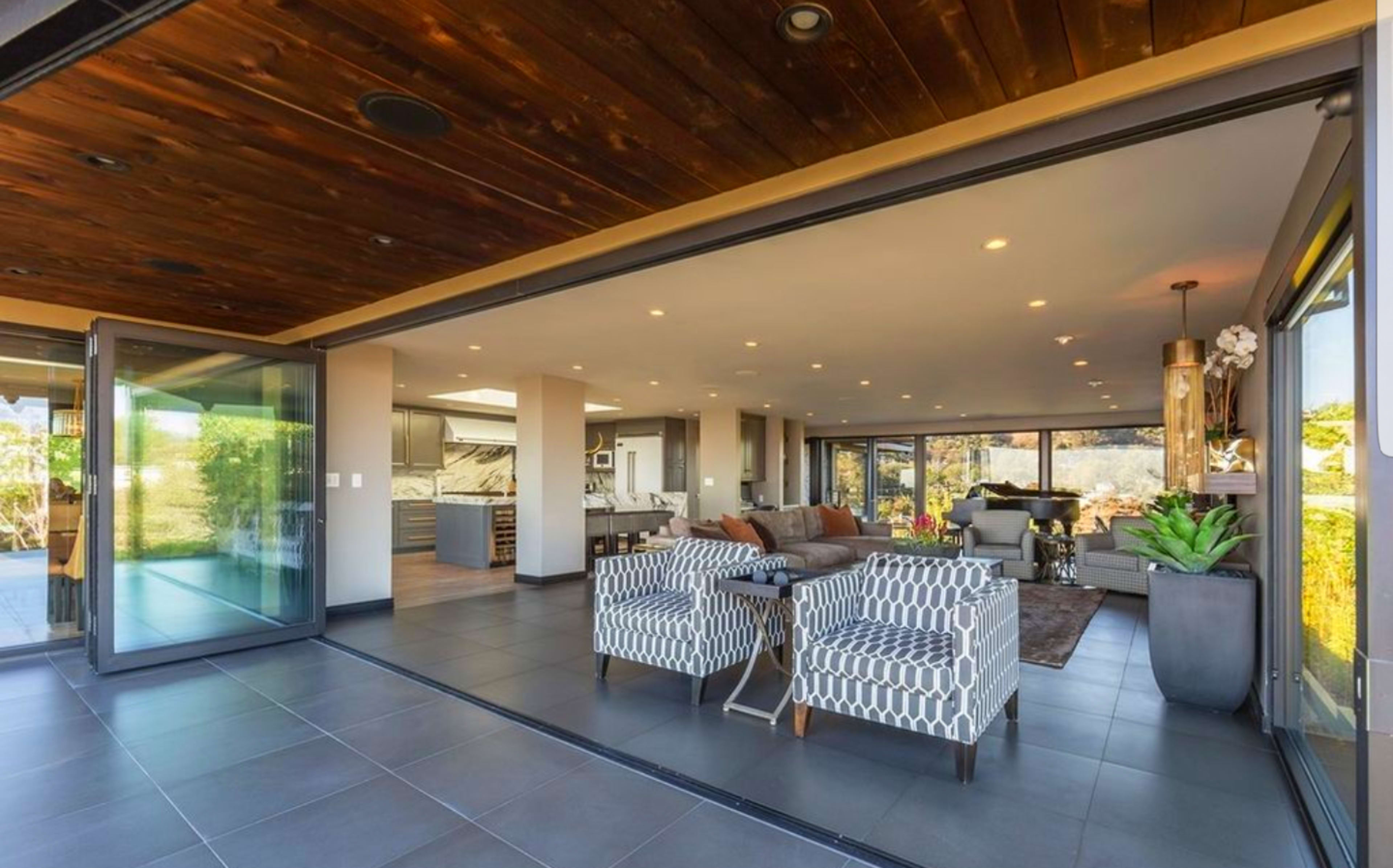A modern living space features an open layout with floor-to-ceiling glass doors that connect the indoor area to an outdoor patio.