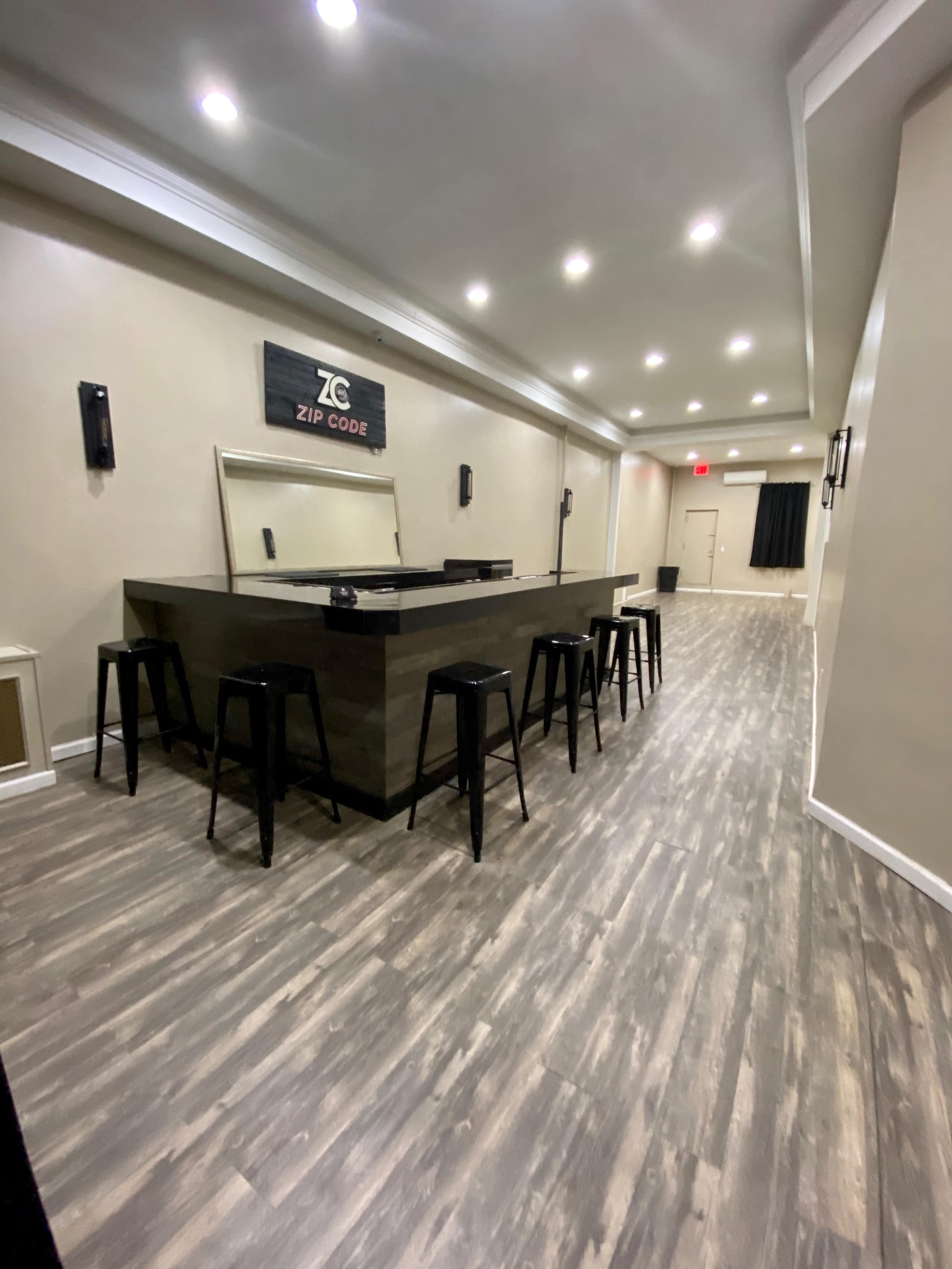 A spacious hallway leading to a bar area with high stools and a sign reading "ZIP CODE" on the back wall.