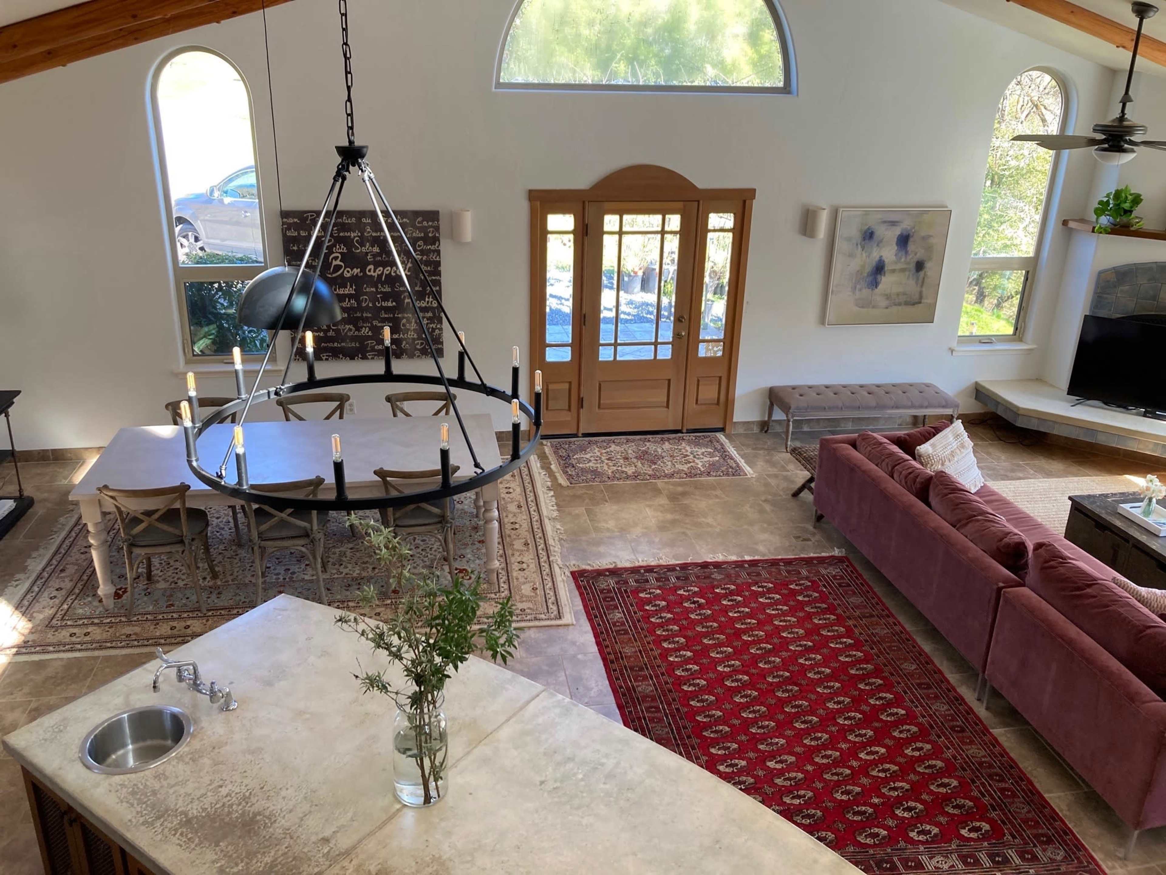 A spacious modern living area with a large dining table, a sectional sofa, and a kitchen island, featuring large windows that provide natural light.