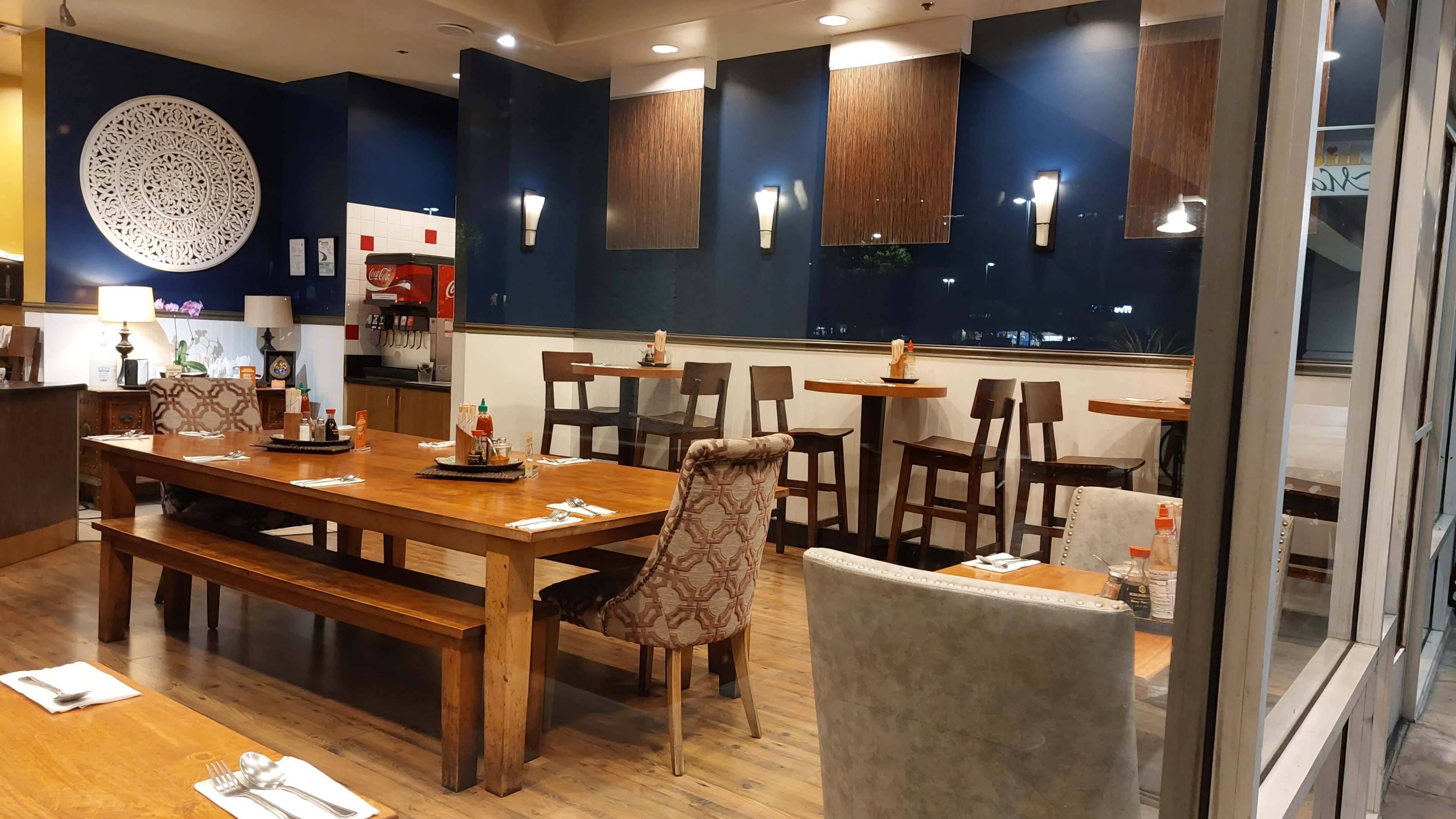 The image shows a restaurant interior featuring wooden tables and chairs, with decorative wall accents and a view through large windows.