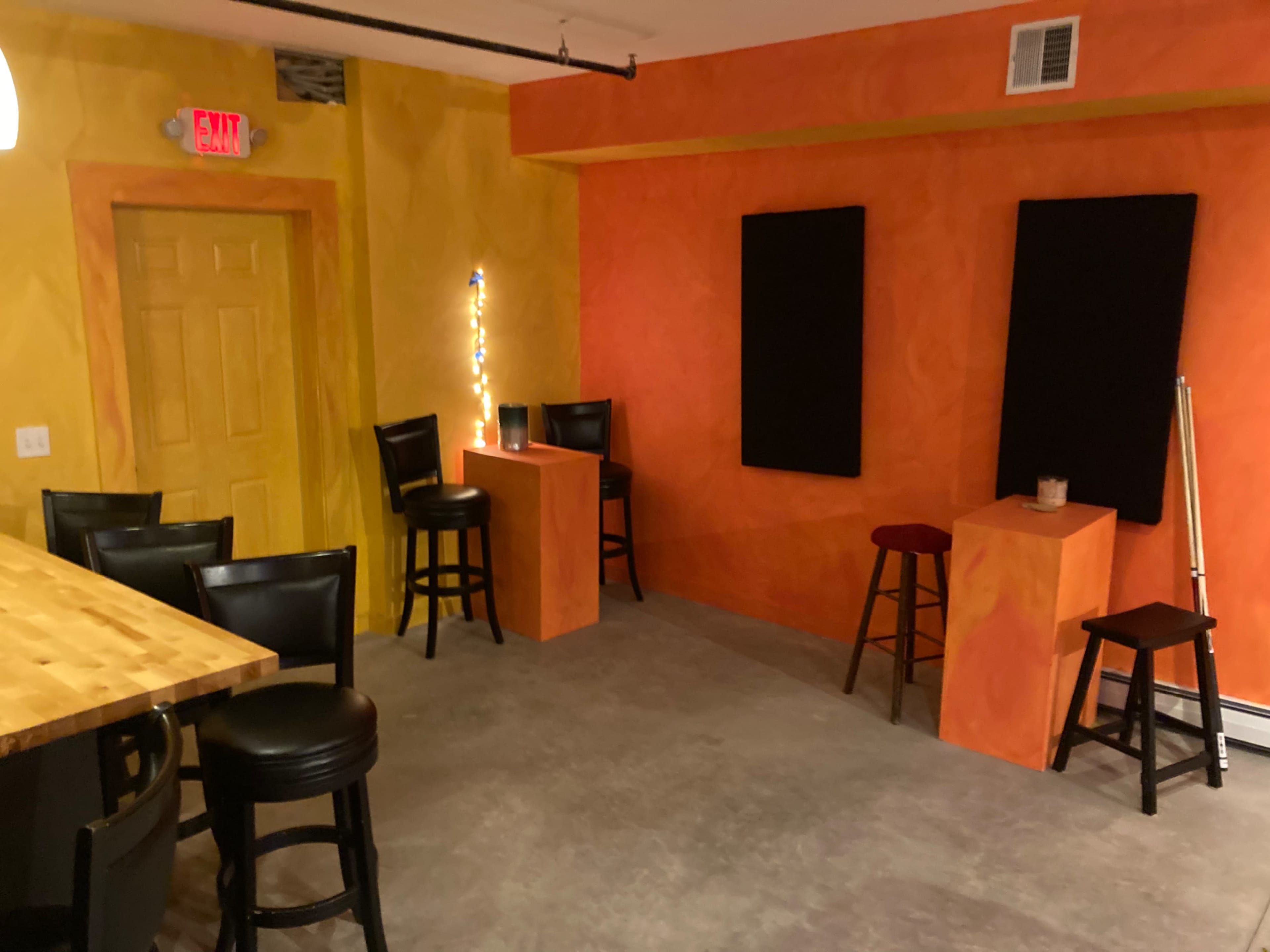 A small room with colorful orange and yellow walls, featuring a bar area with black stools and a couple of elevated tables.