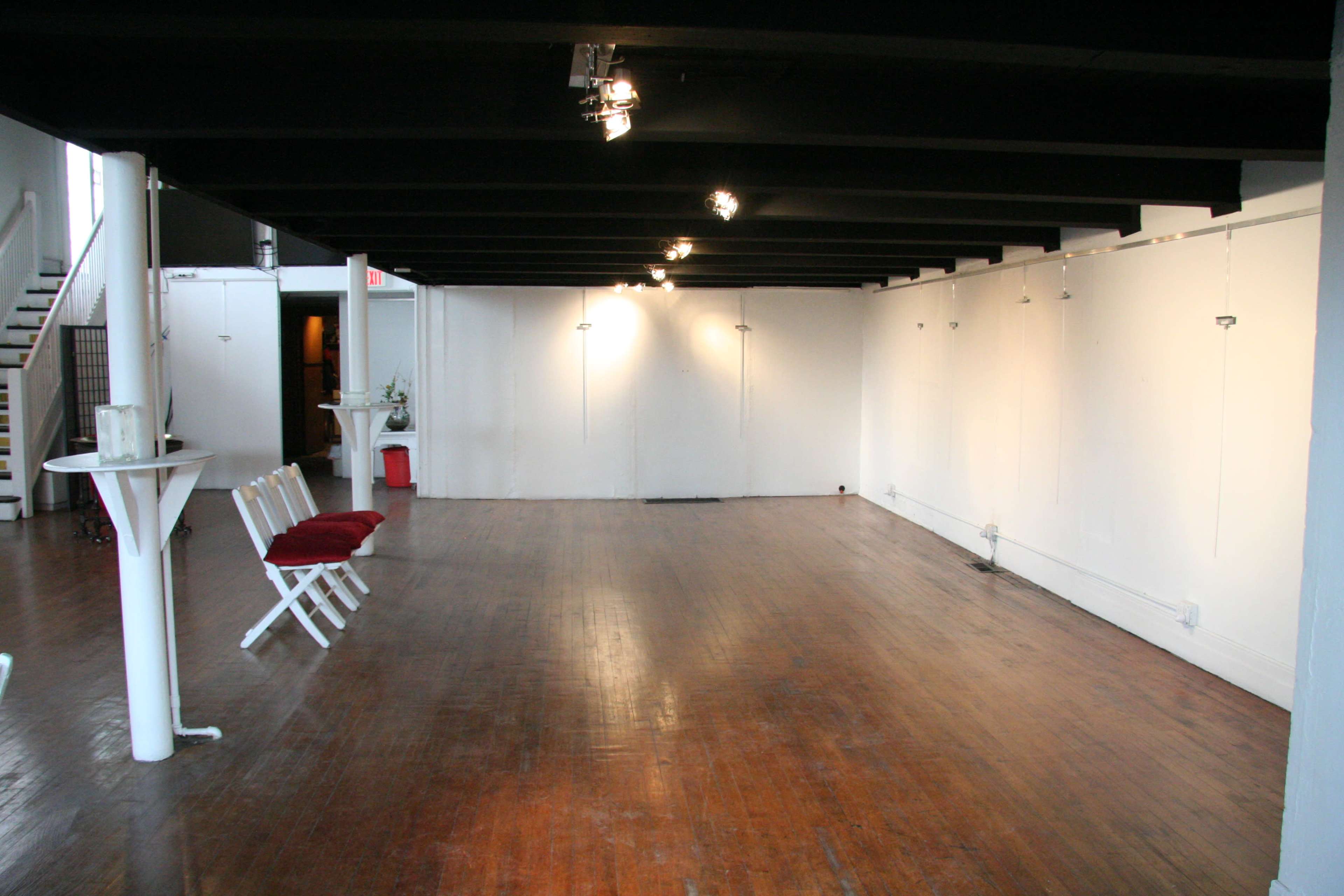 A spacious, empty gallery with wooden floors and white walls, featuring minimal seating and track lighting.
