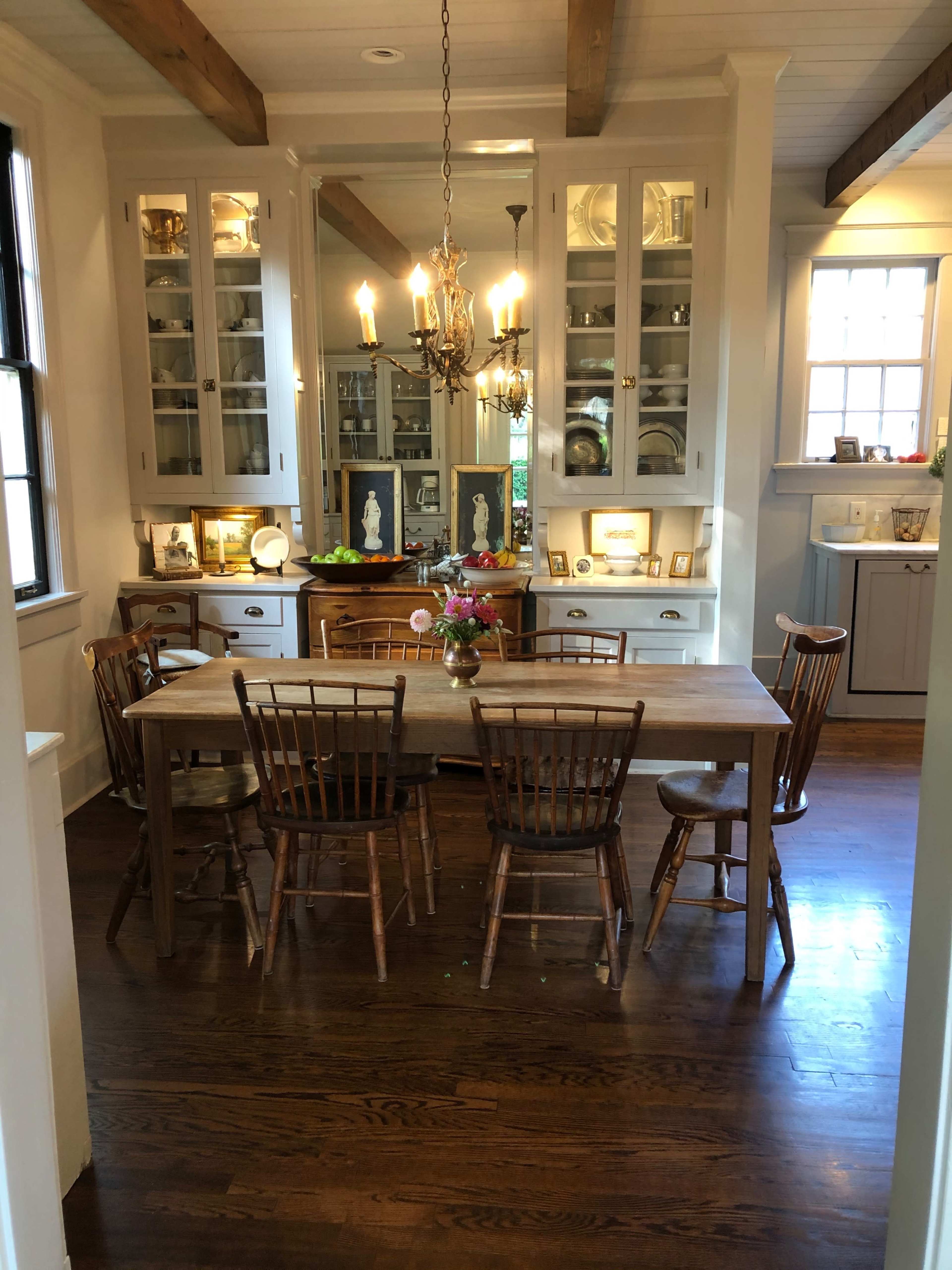 A wooden dining table surrounded by chairs is set in a well-lit room featuring glass-front cabinets and a chandelier.