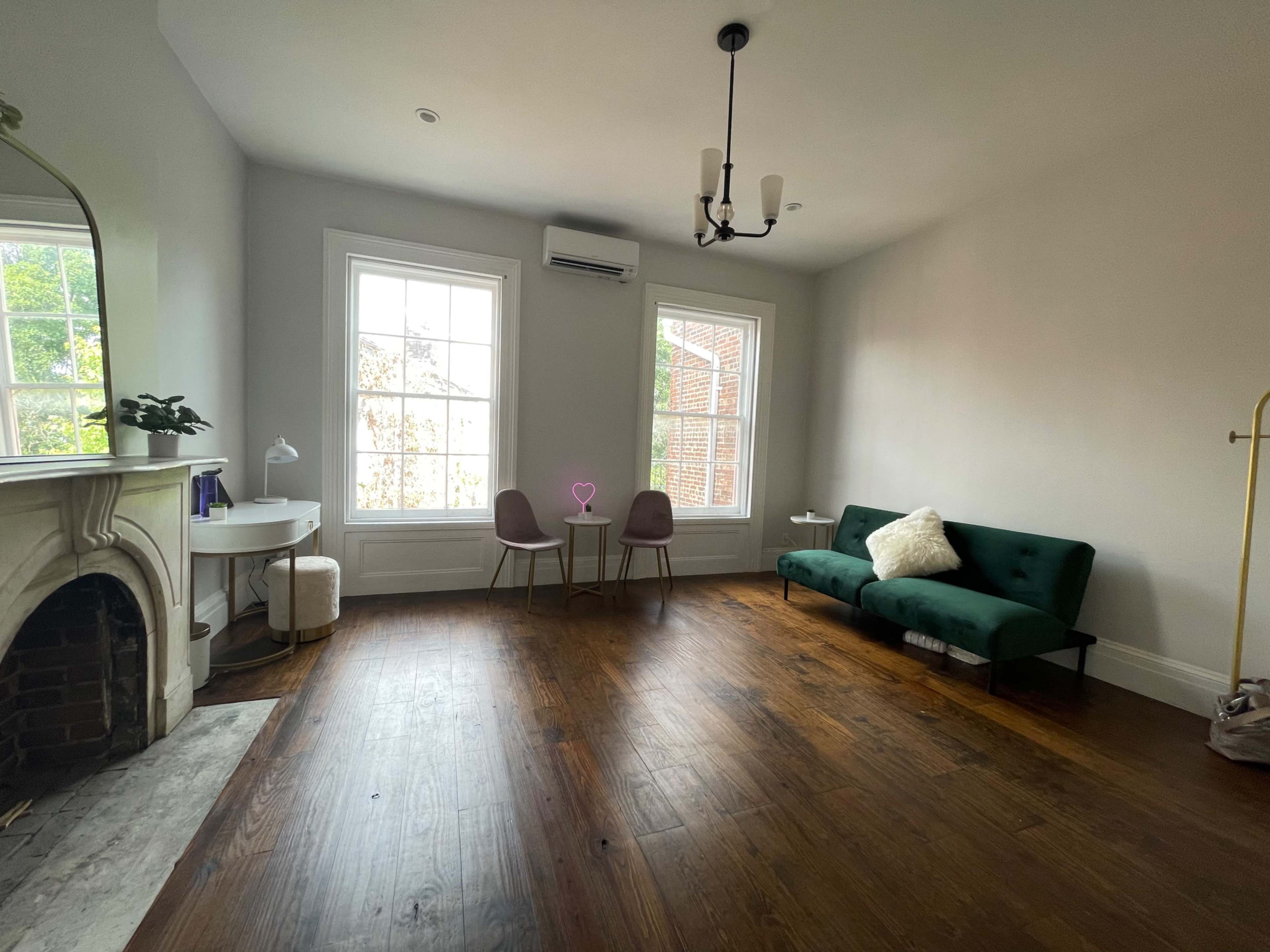 The room features a green couch, two chairs, a small table, and large windows with natural light pouring in.