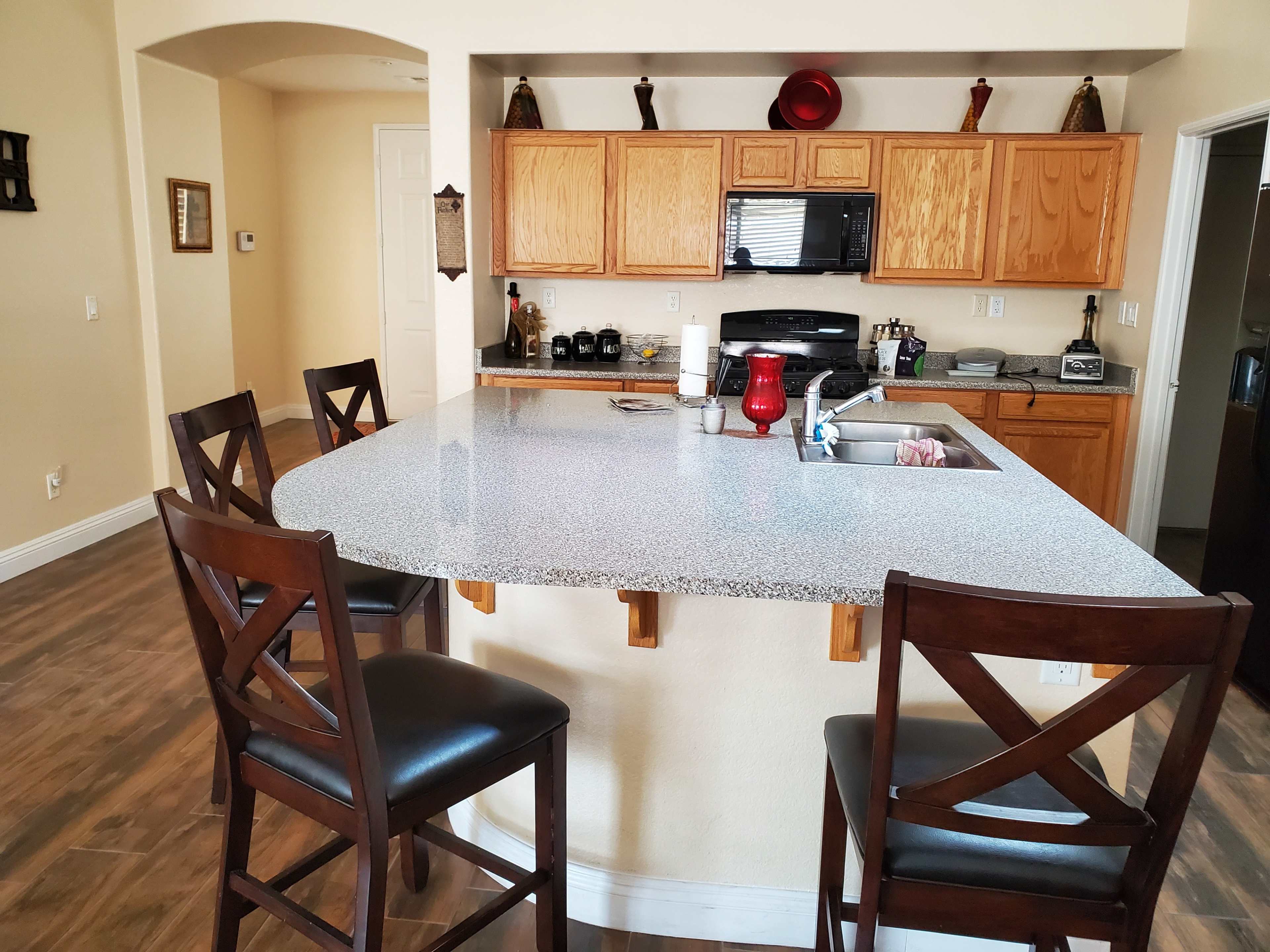 A modern kitchen with wooden cabinets, a granite countertop island, and four brown bar stools.