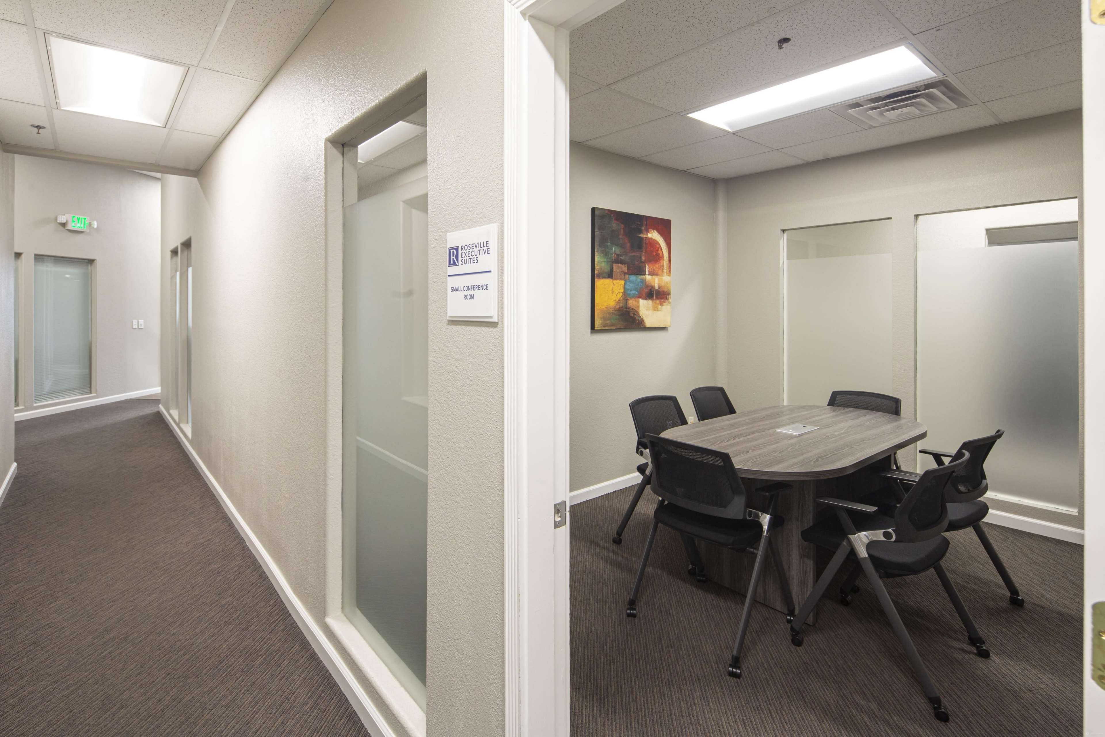 The image shows a well-lit hallway leading to a conference room with a large table and chairs.