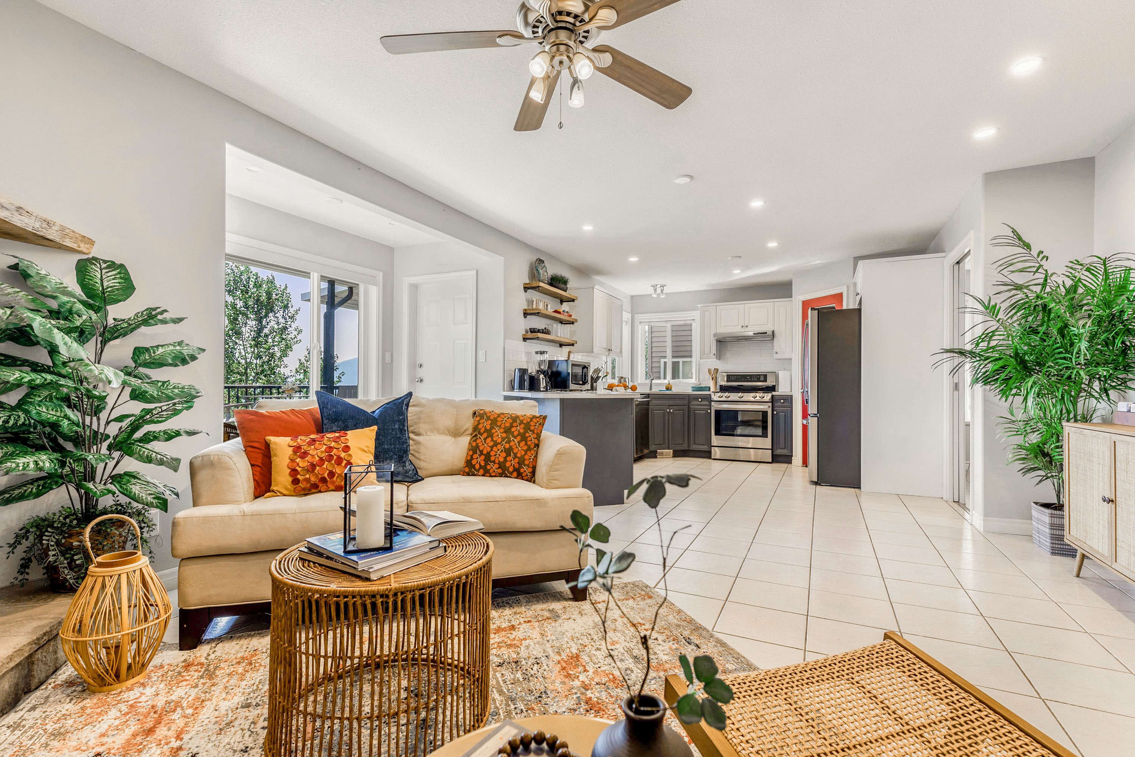 A bright living room features a beige sofa, a round wicker coffee table, and a kitchen area in the background with modern appliances.
