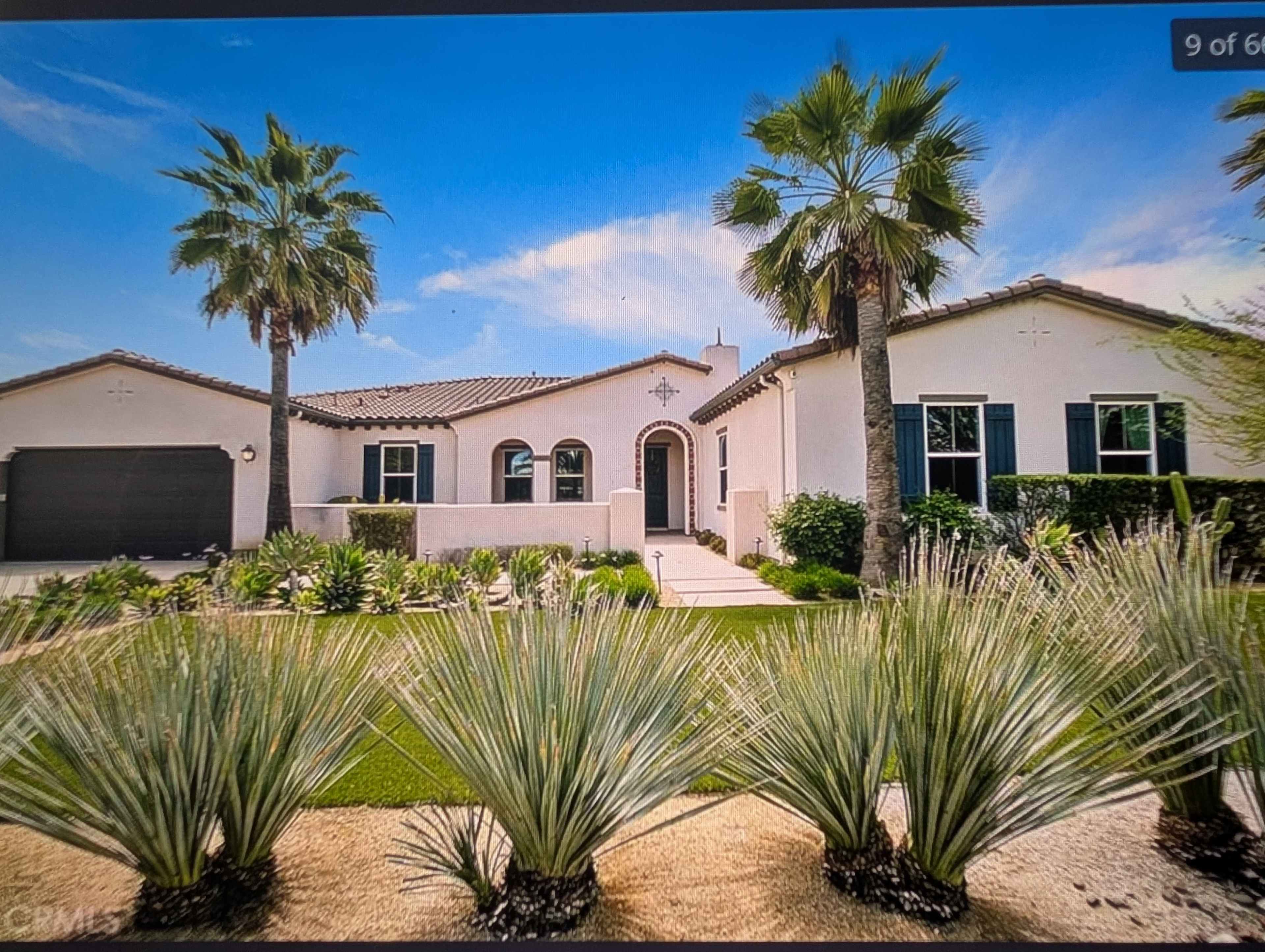 The image shows a single-story, modern home with a tiled roof, surrounded by palm trees and desert landscaping.