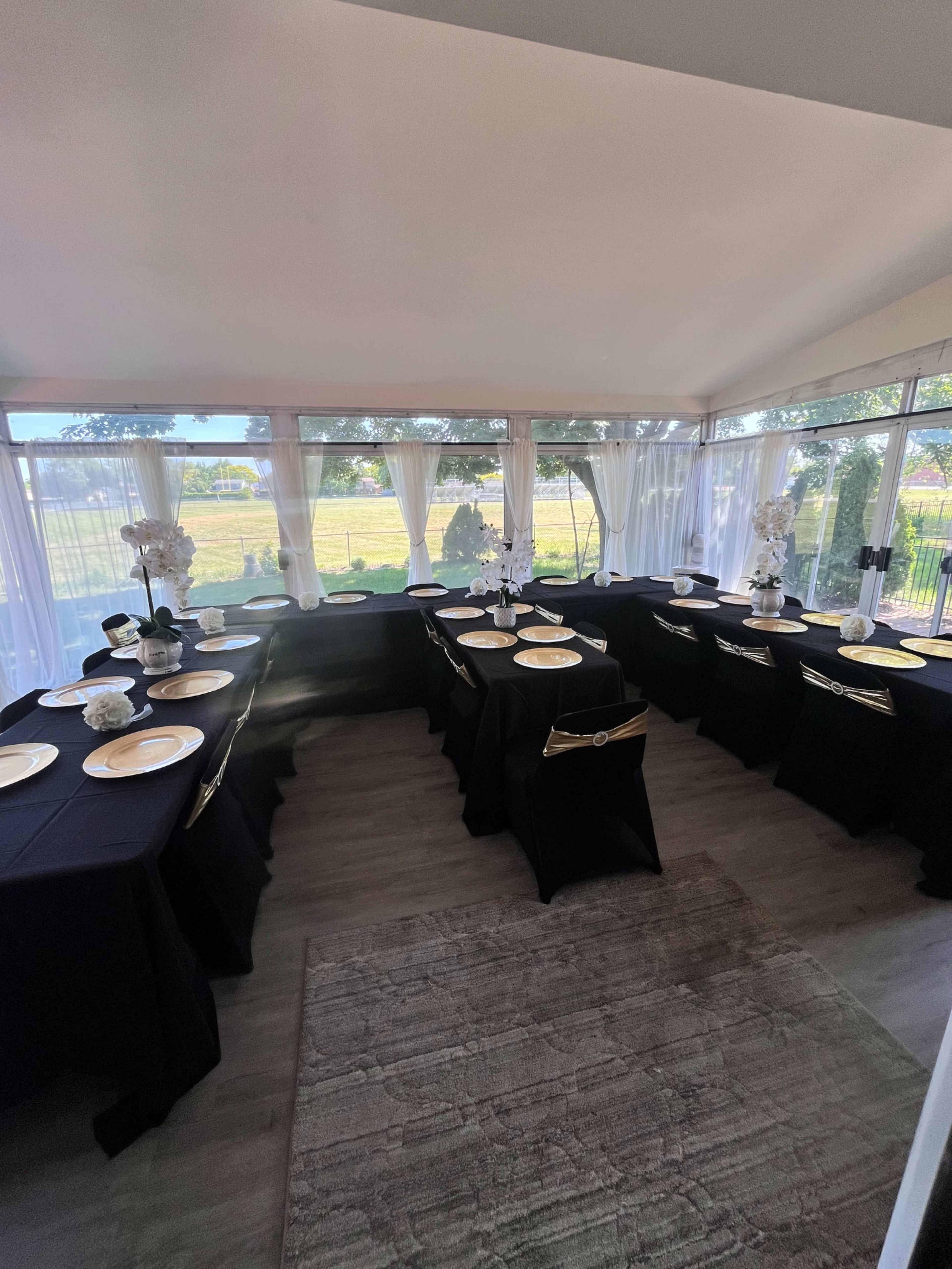 A banquet room is set up with black tablecloths and white plates, featuring large windows that overlook a scenic outdoor area.