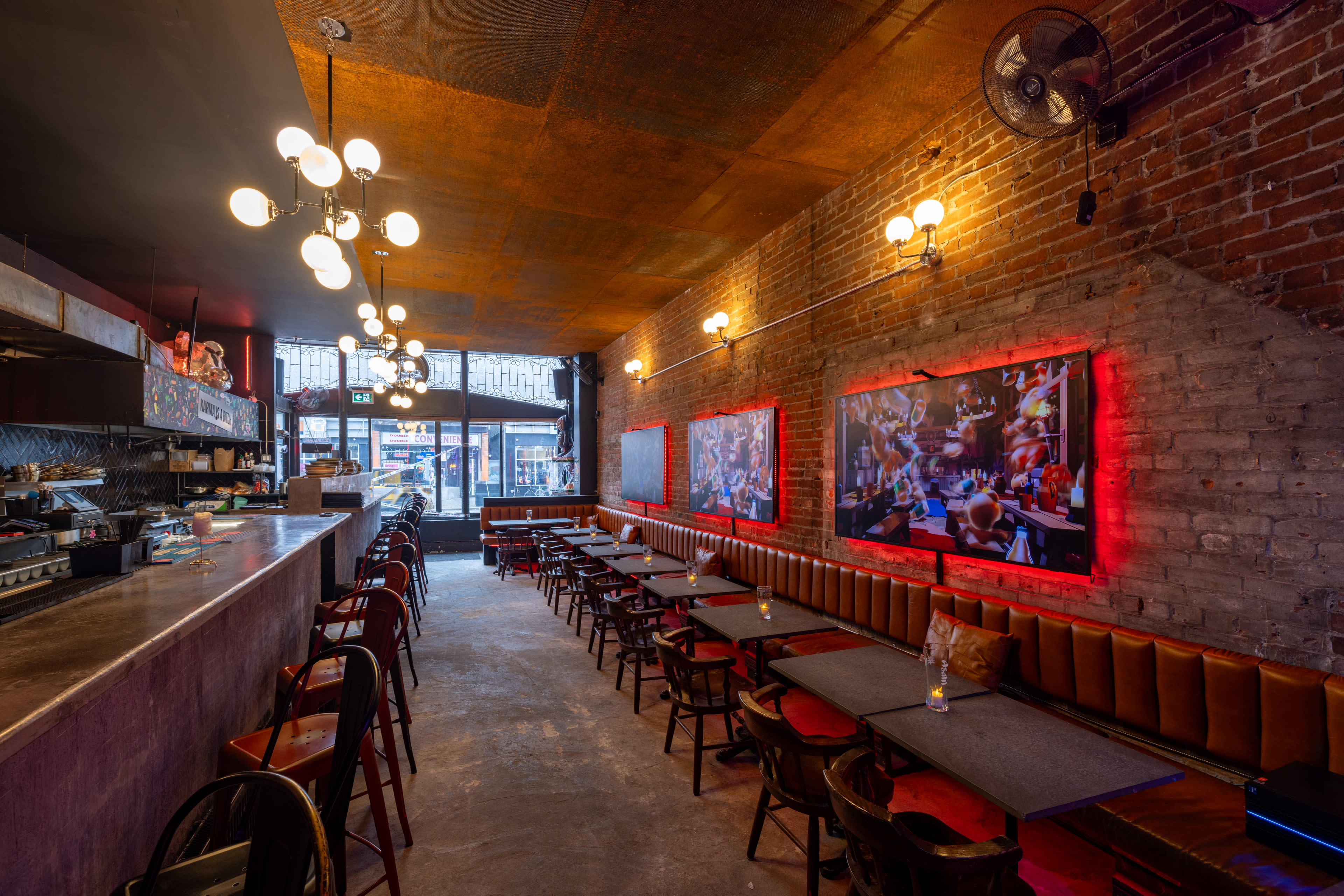 The interior of a restaurant features exposed brick walls, illuminated artwork, and rows of tables with wooden chairs.