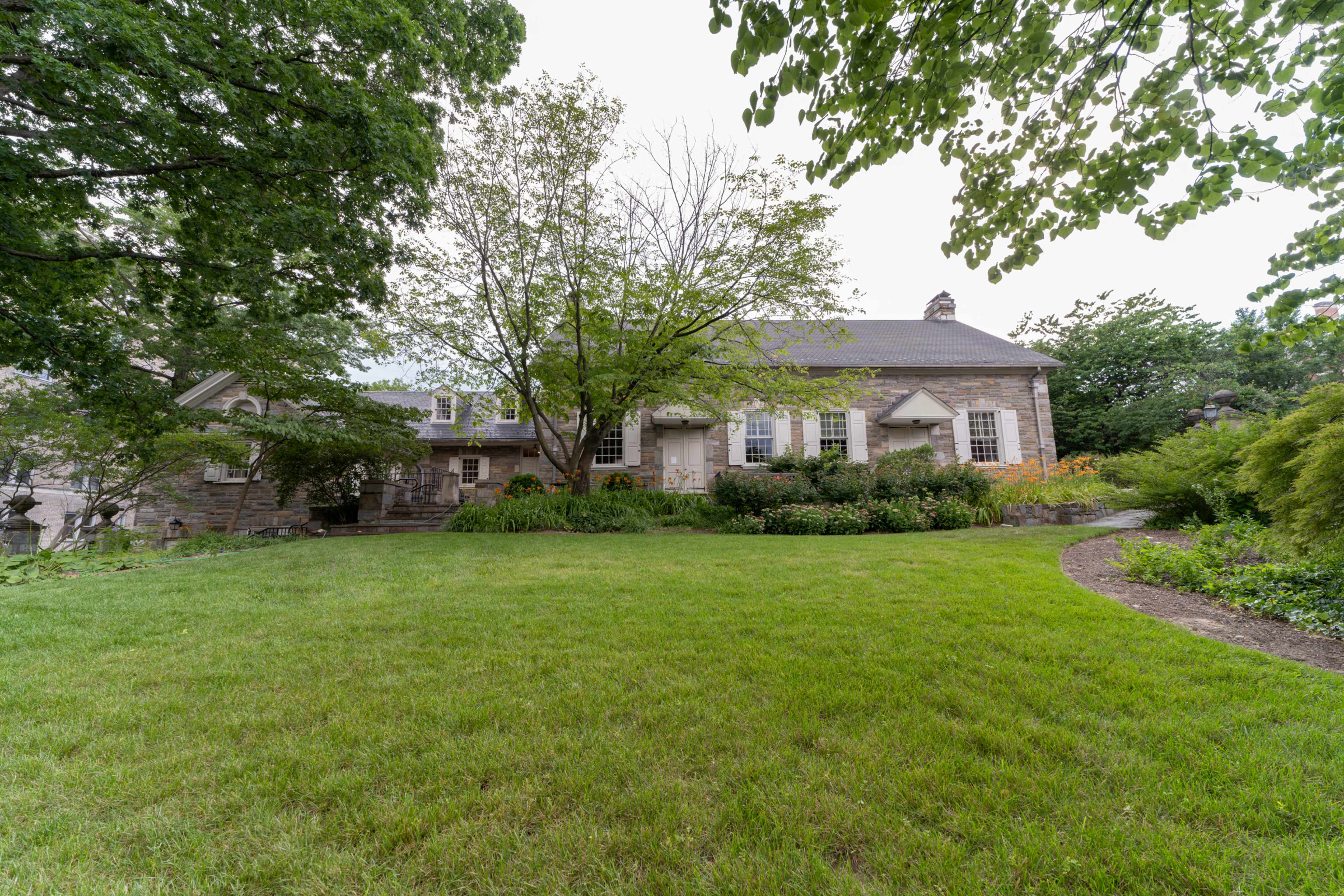 A large stone house set in a green lawn surrounded by trees and garden plants.