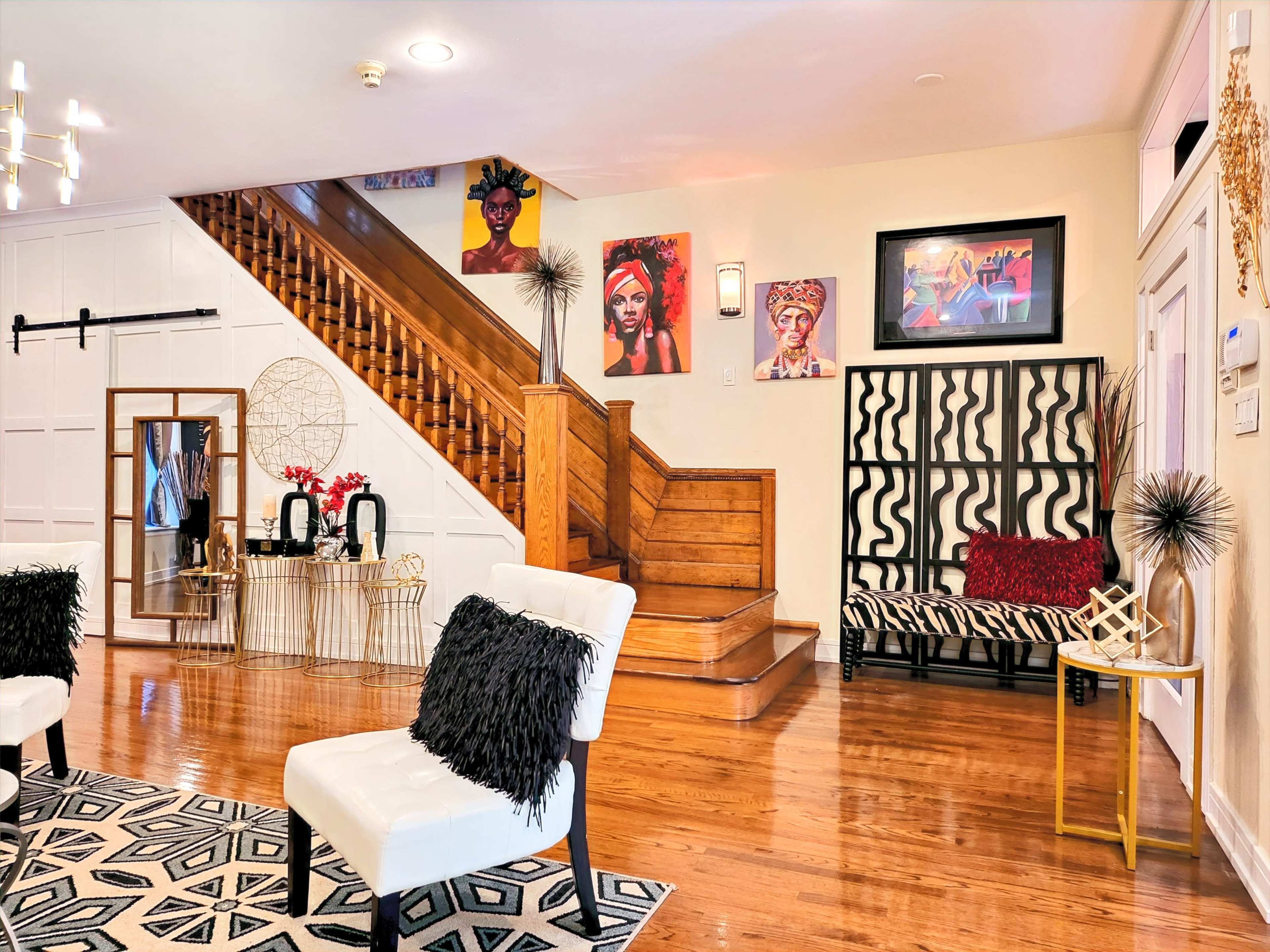A well-lit entryway featuring a staircase, a decorative wall with artwork, and stylish seating arrangements.
