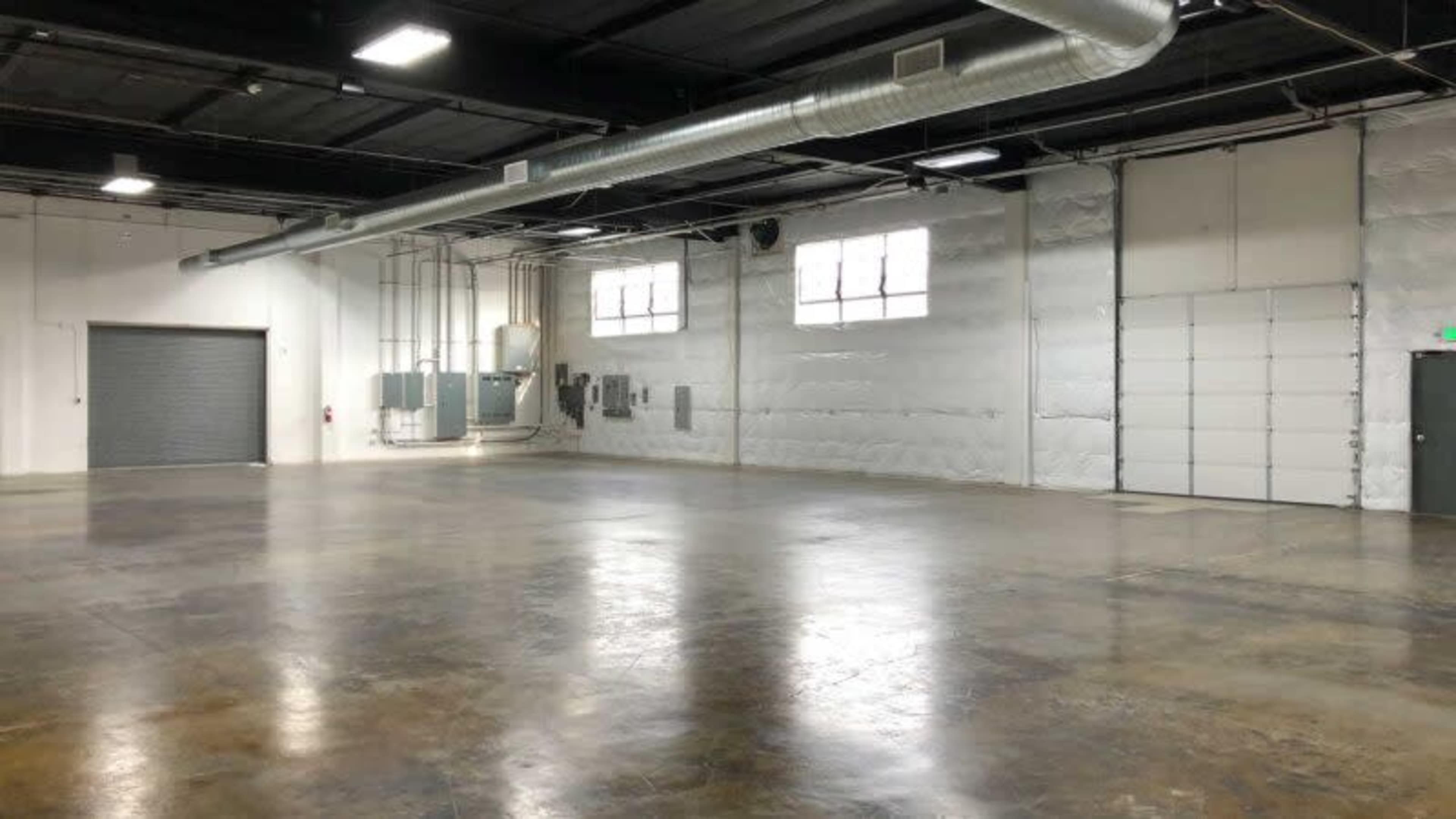 An empty industrial space with polished concrete floors, large windows, and a roll-up garage door on one side.