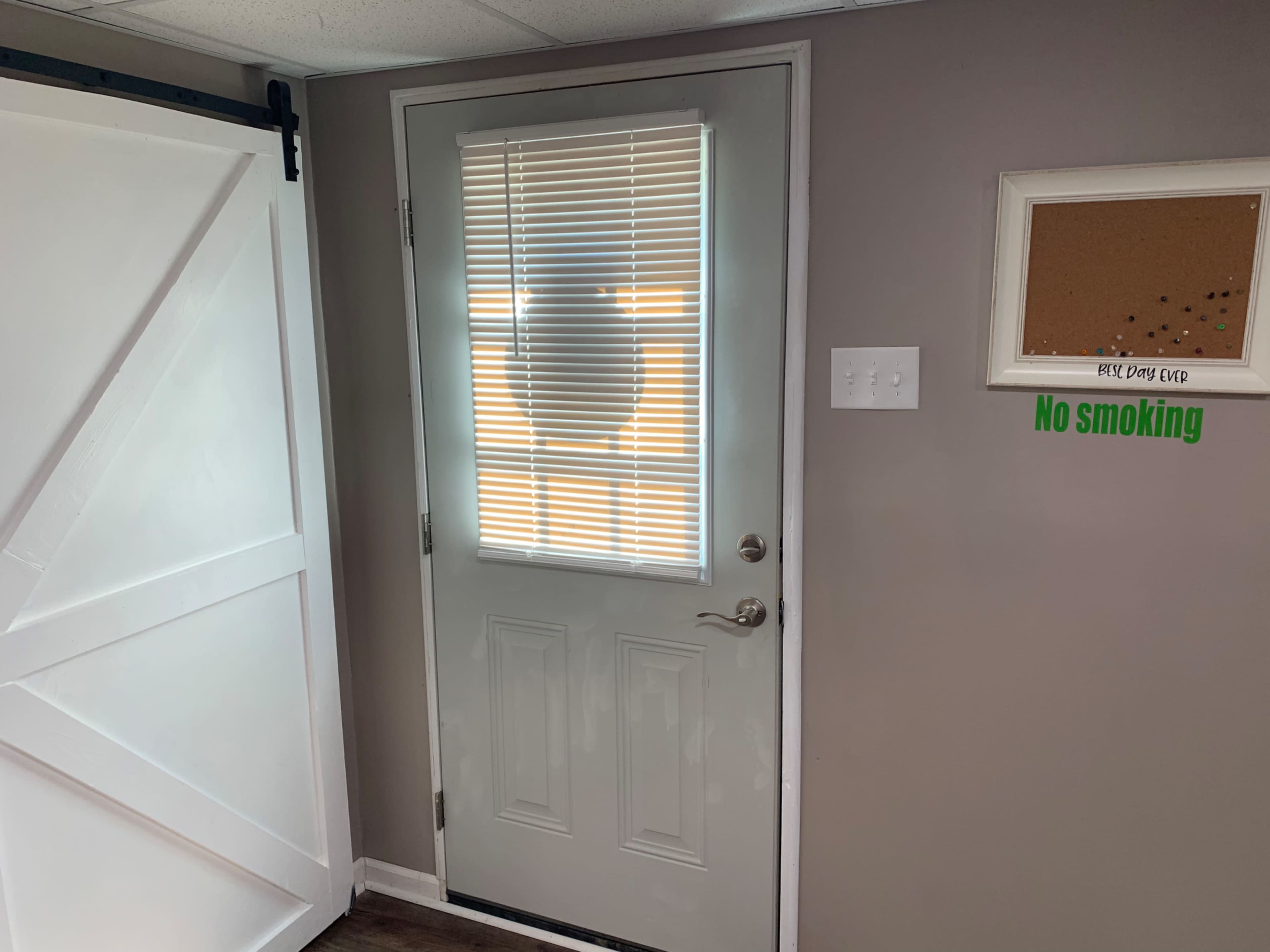 A light-colored door with blinds partially closed, adjacent to a sliding barn door and a wall displaying a "No smoking" sign.