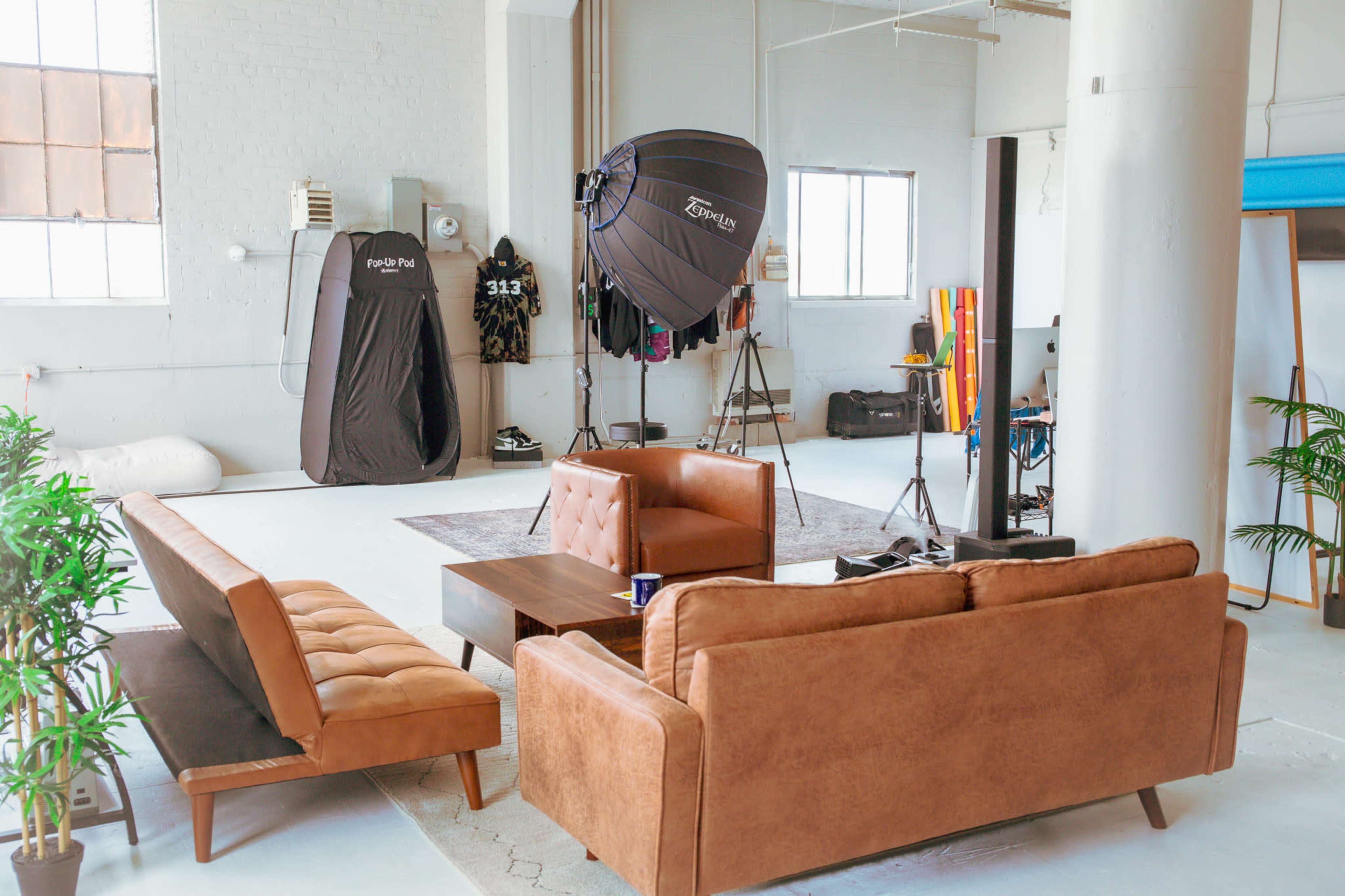 A spacious studio with two brown sofas, a coffee table, and a large softbox lighting setup in a well-lit environment.
