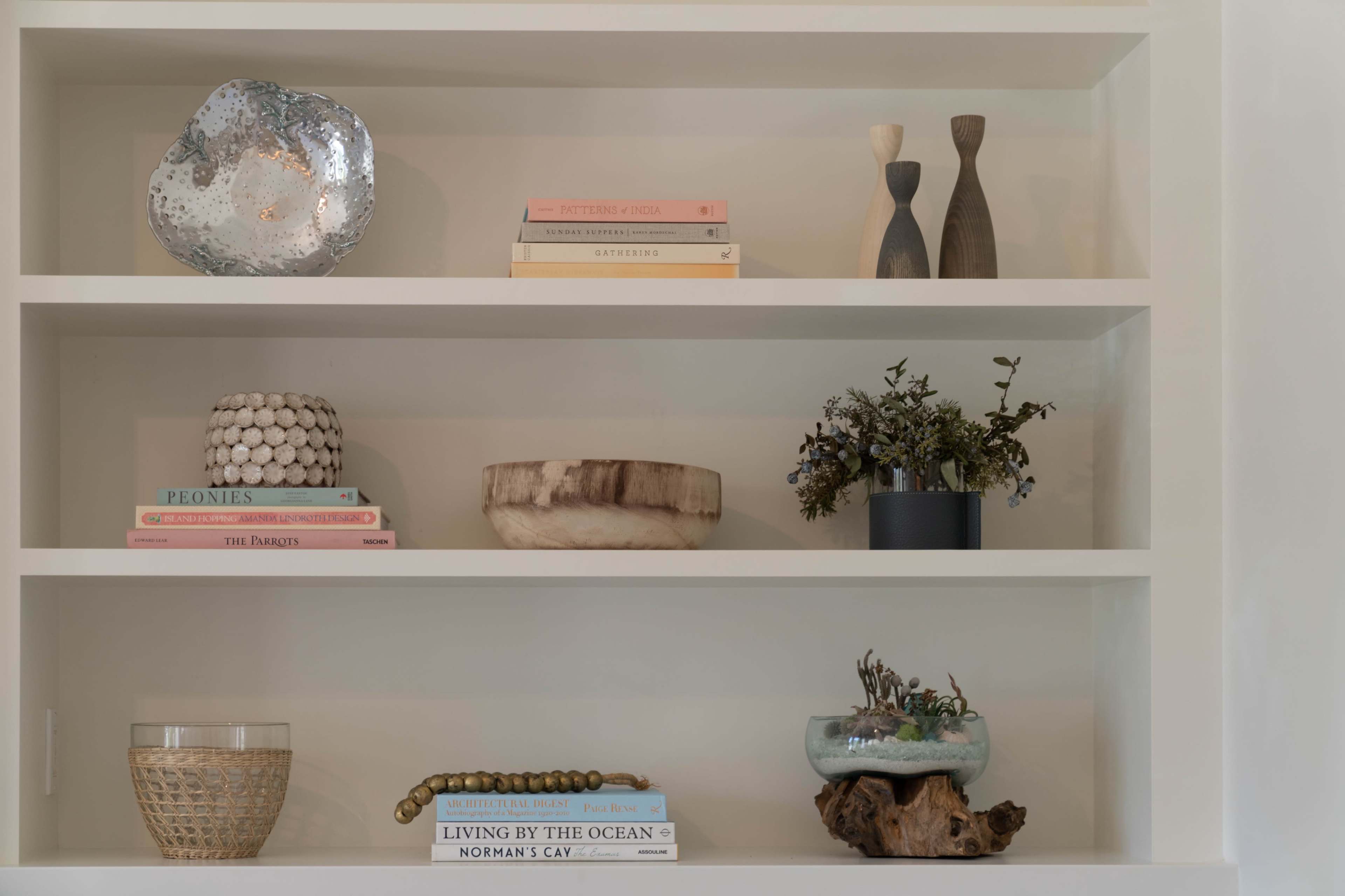 The image shows a neatly organized shelf displaying a variety of decorative items, including books, a metallic bowl, and small plants.