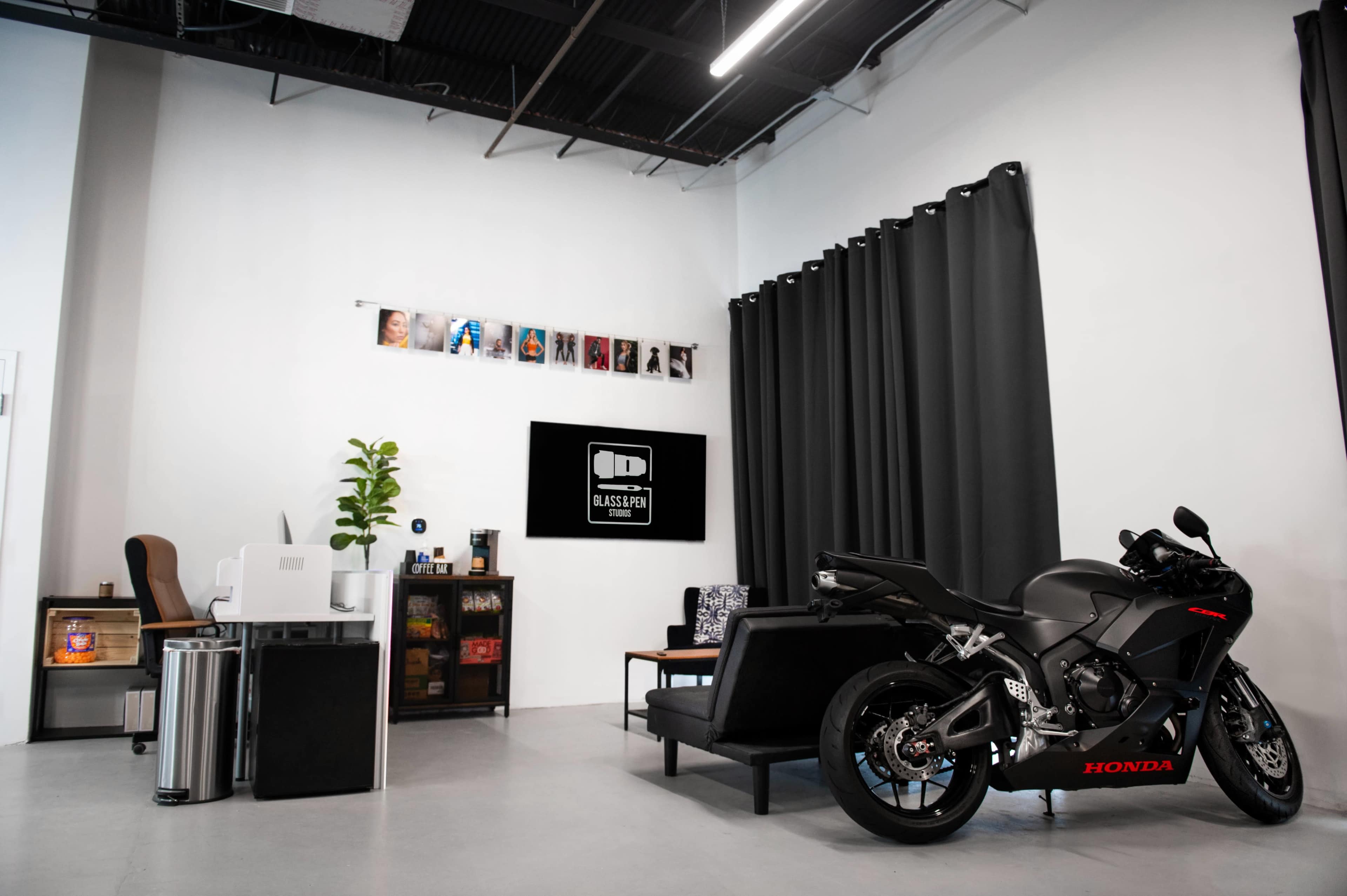 A sleek black motorcycle is parked beside a modern couch in a well-lit room featuring dark curtains and a television display.