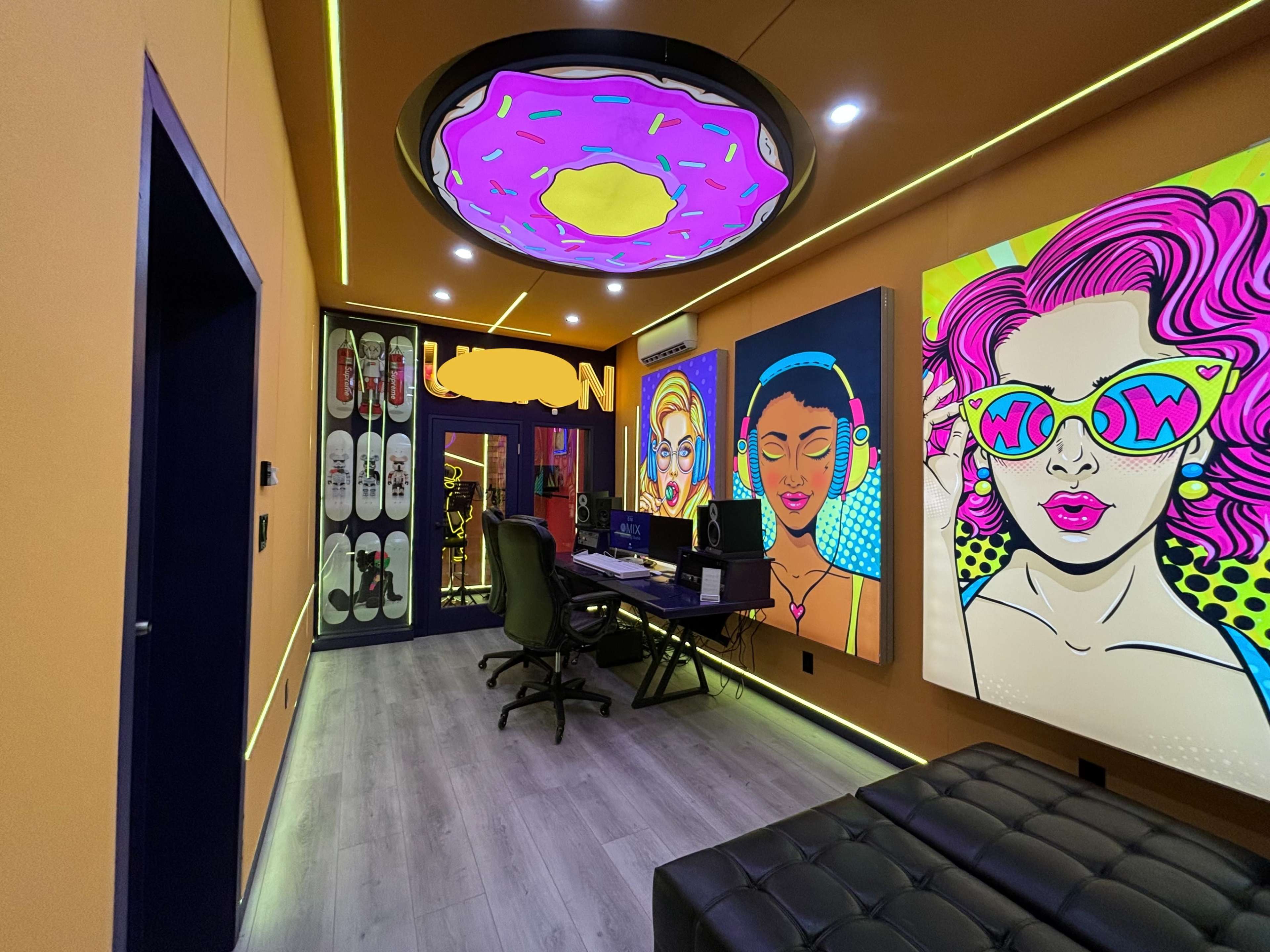 The room features vibrant, colorful artwork on the walls, a desk with computers, and a unique ceiling design that resembles a doughnut.