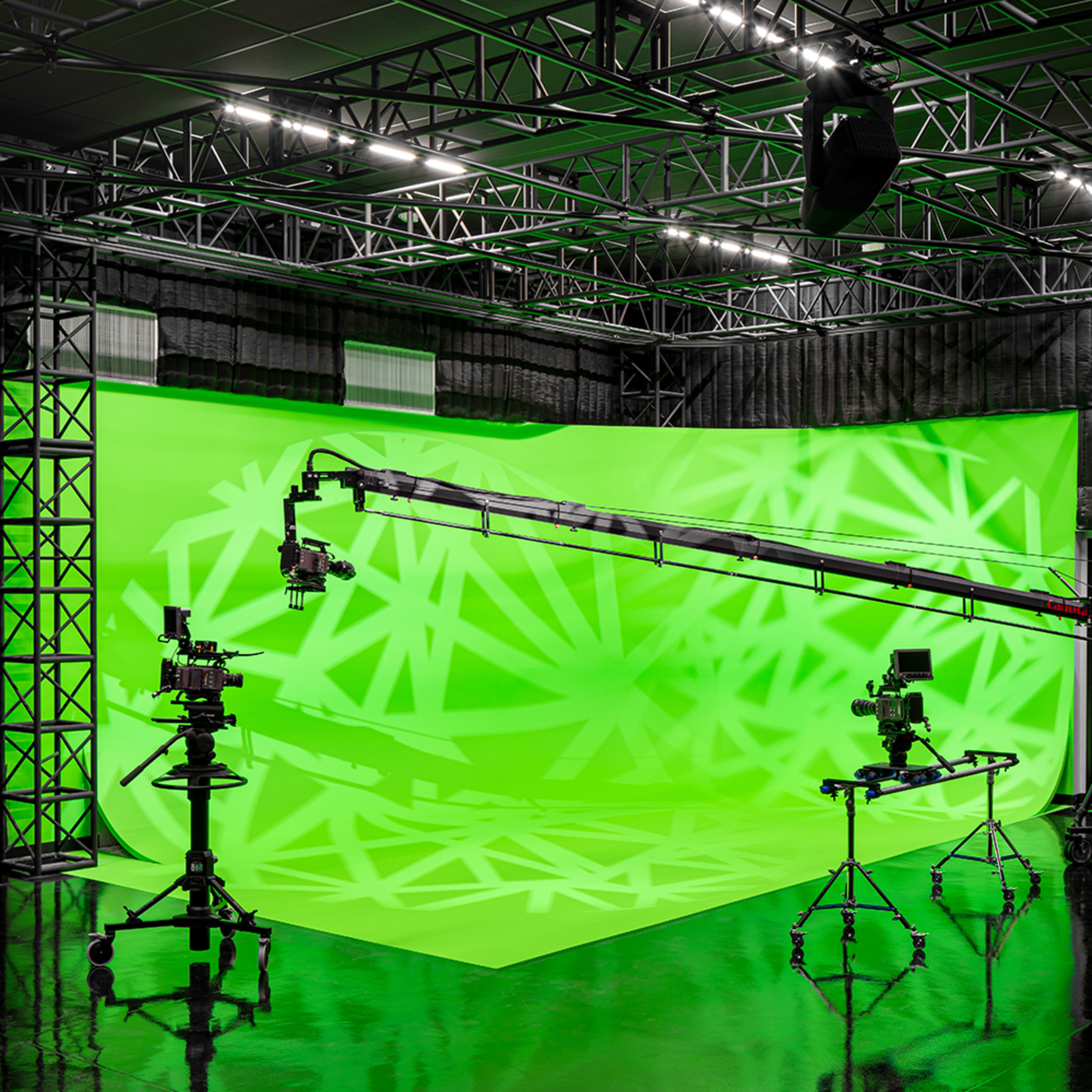 A film studio with green screens and camera equipment arranged on a reflective floor.