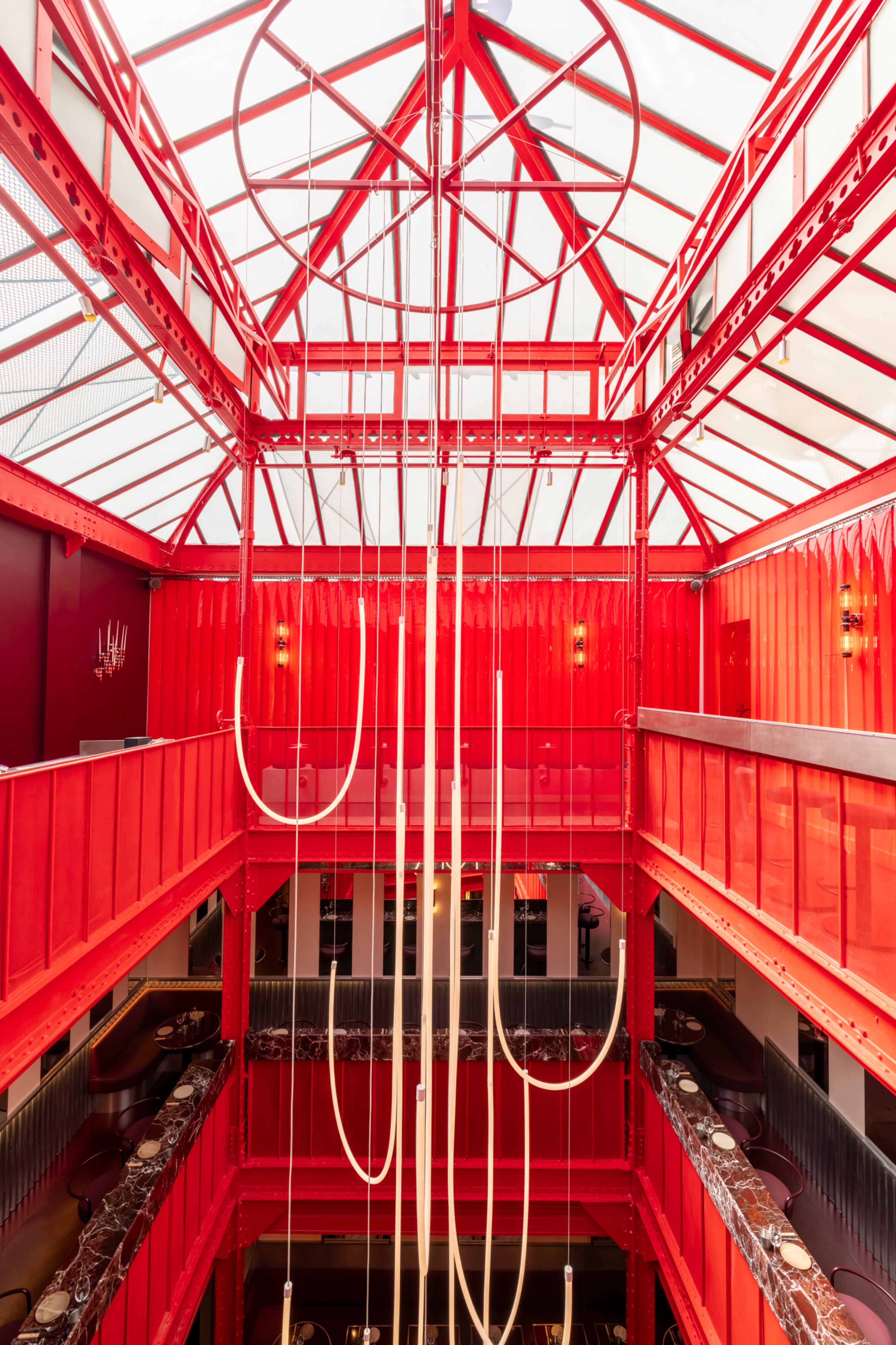The image shows an indoor space of a restaurant characterized by a bright red interior and a large, intricate ceiling structure with hanging light fixtures.